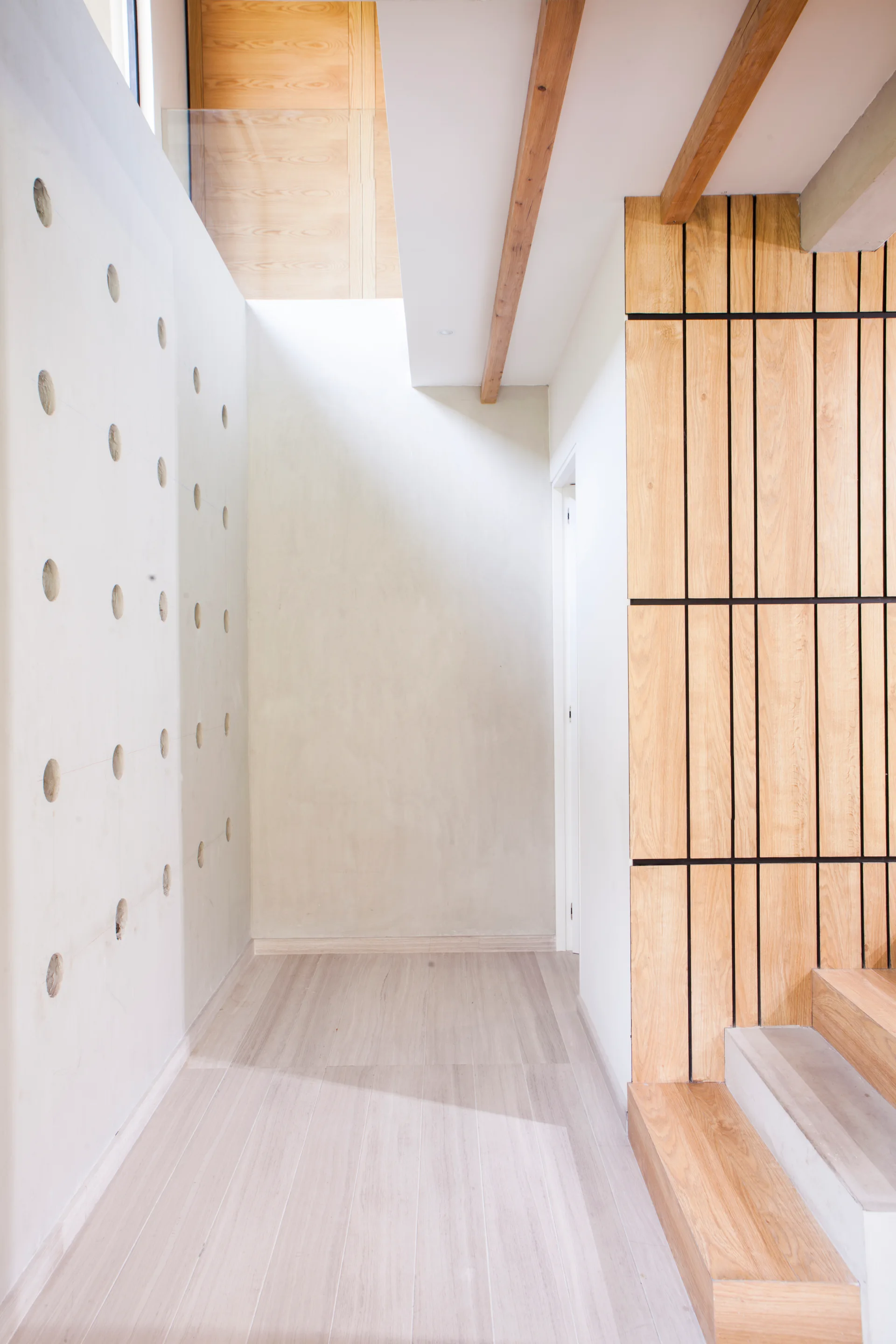 A modern, bright hallway featuring a smooth concrete wall with decorative circular indentations alongside warm wood slat paneling.