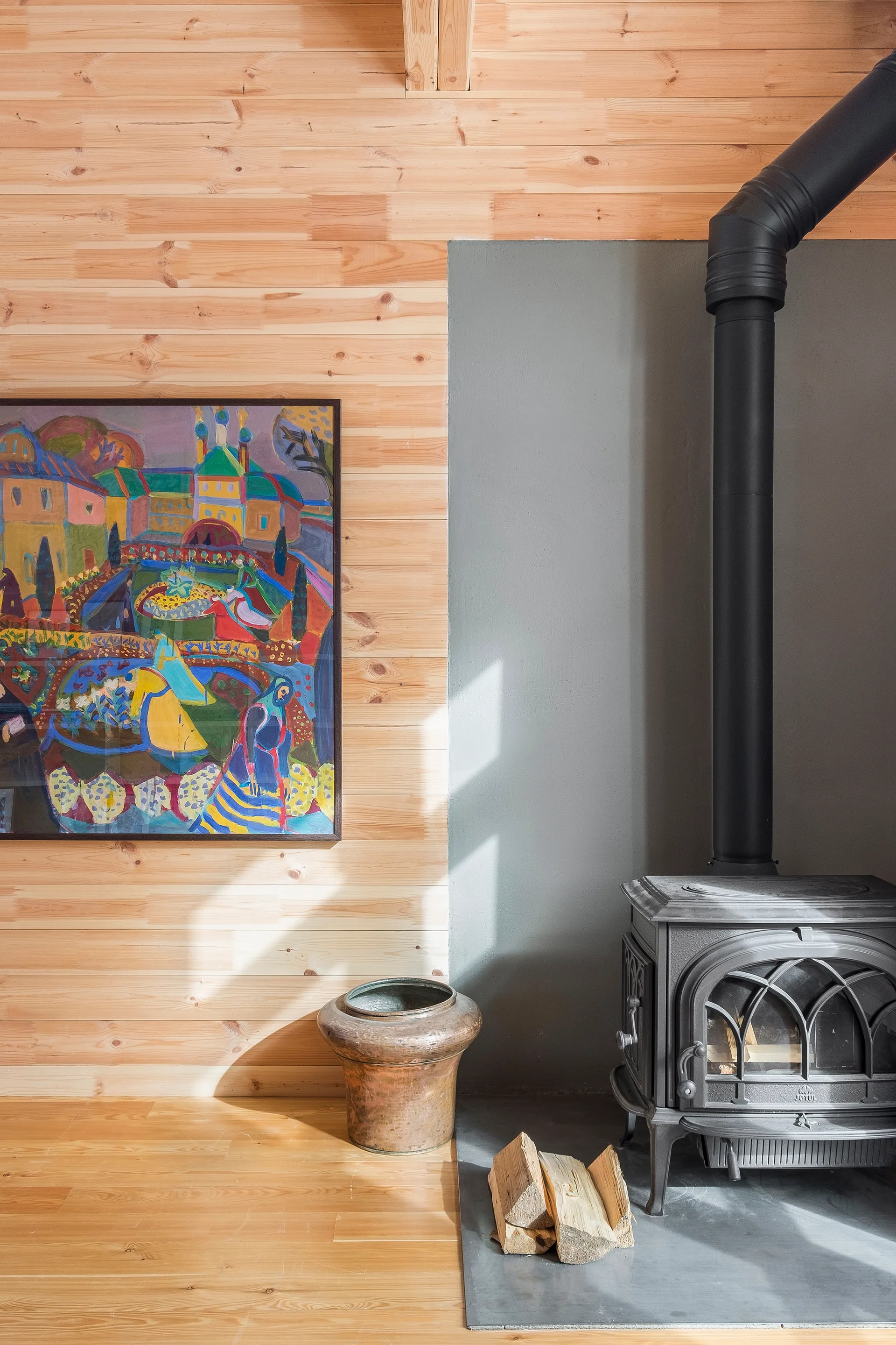 A black cast iron wood burning stove sits on a grey hearth against a wall split between light wood paneling and matte grey paint.