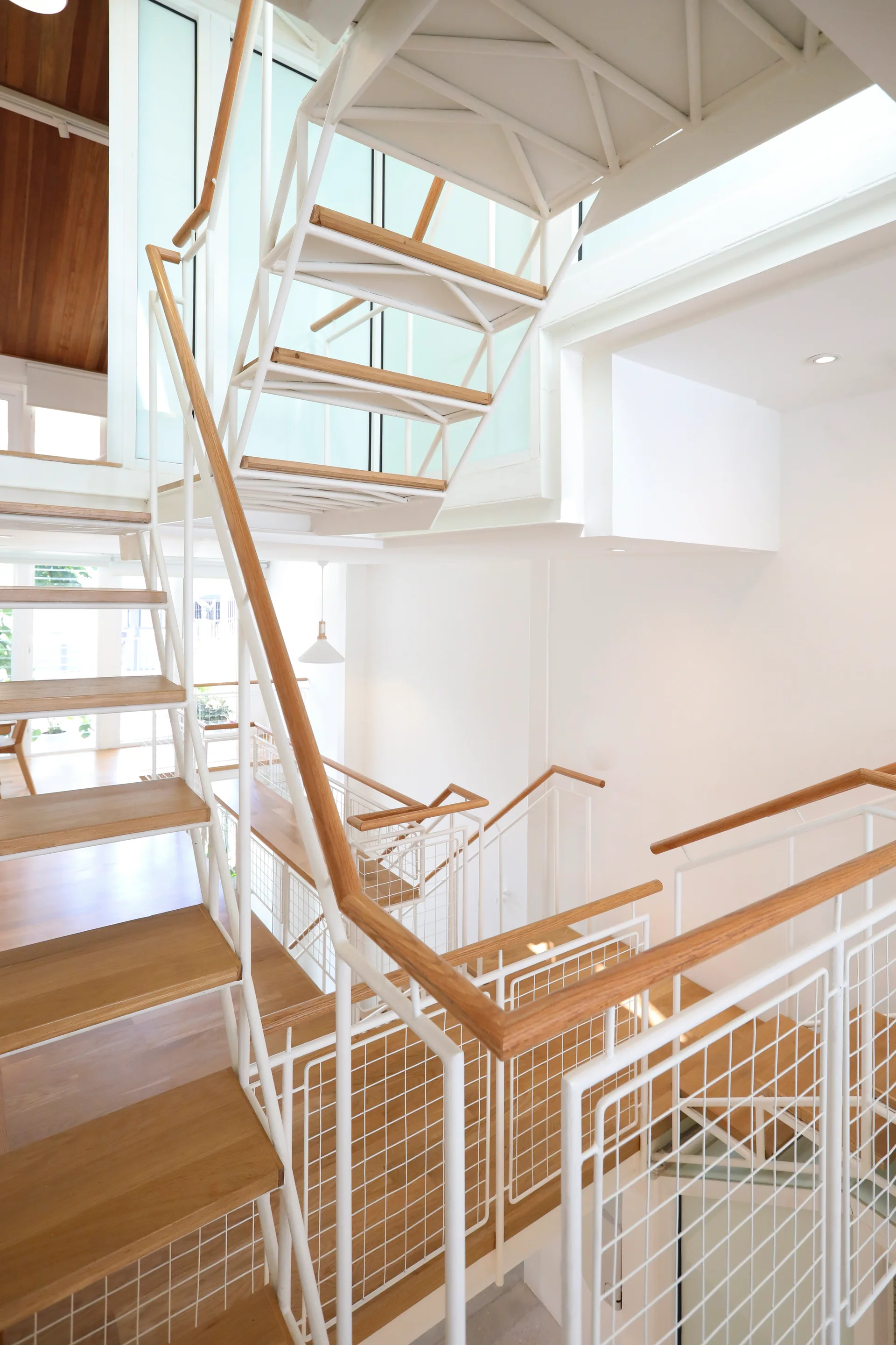 A multi-level white metal staircase features open-riser wood treads, mesh grid railings, and smooth wooden handrails in a bright, minimalist interior.