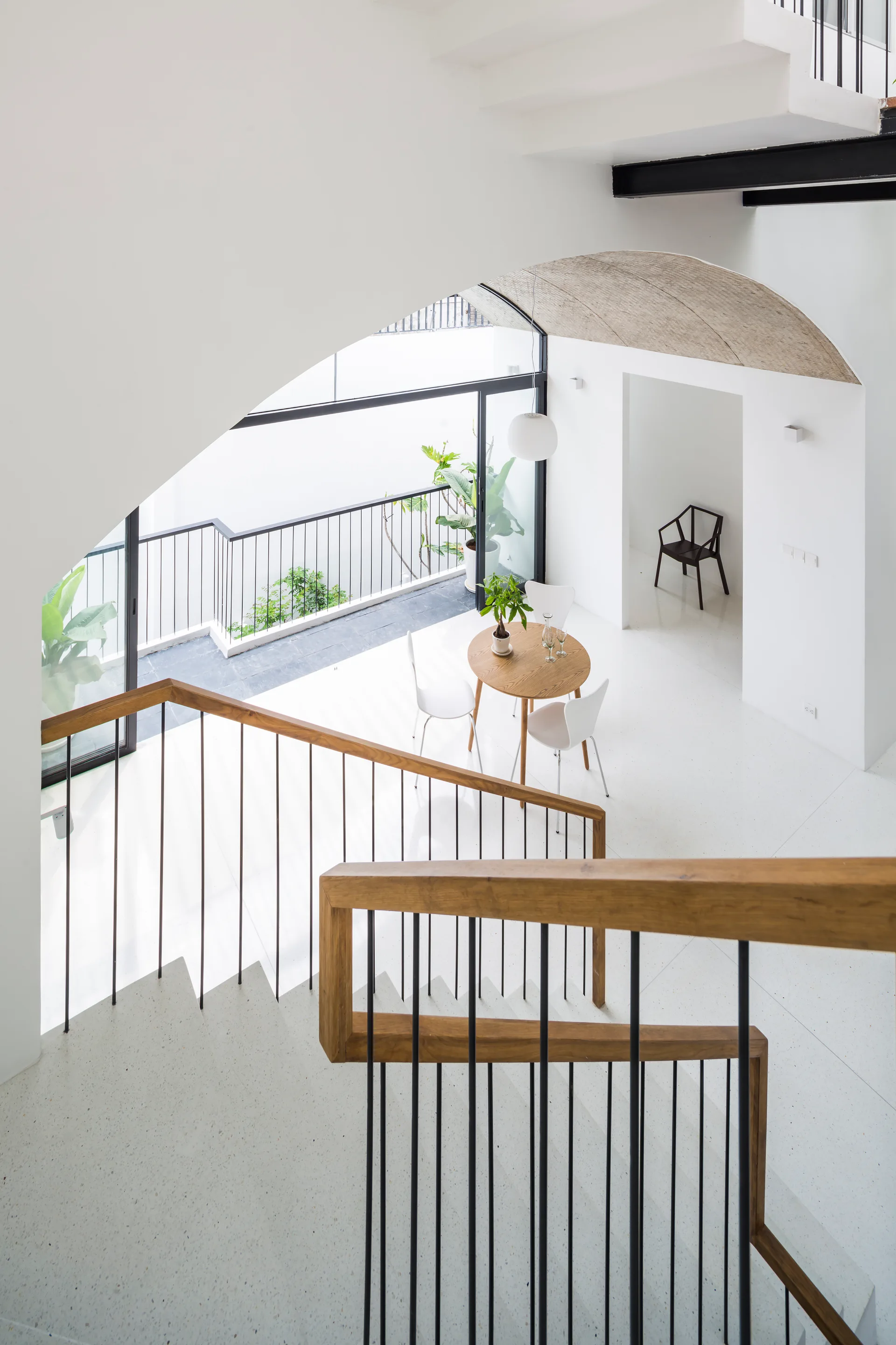 A high-angle view of a modern white staircase with wood railings looking down onto a minimalist dining table set near large sliding glass doors.