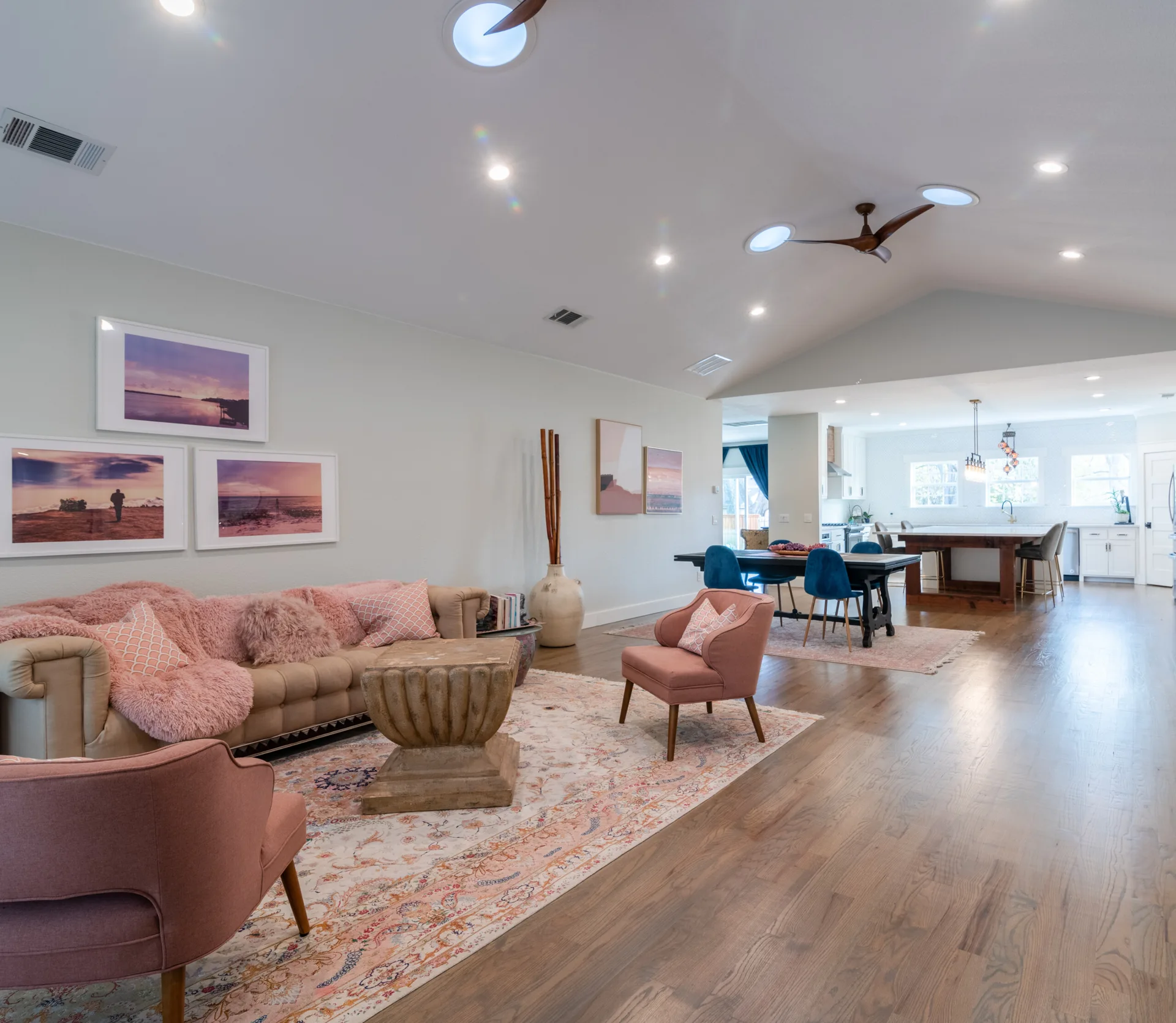 An open-concept living room features a beige sofa, pink armchairs, a carved wooden coffee table, and circular skylights in a vaulted ceiling.