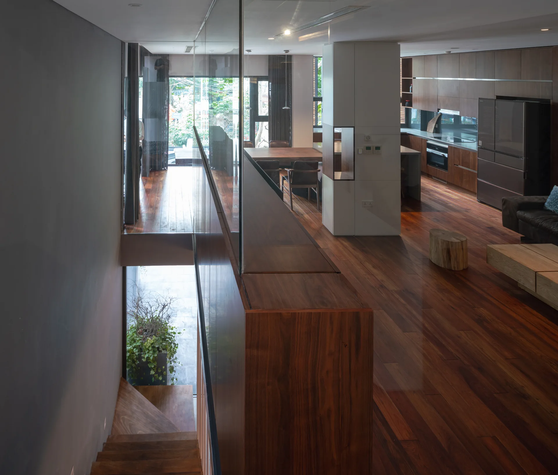 A modern open-plan home featuring rich hardwood floors, a staircase with a glass partition, dark wood kitchen cabinetry, and a dining area.
