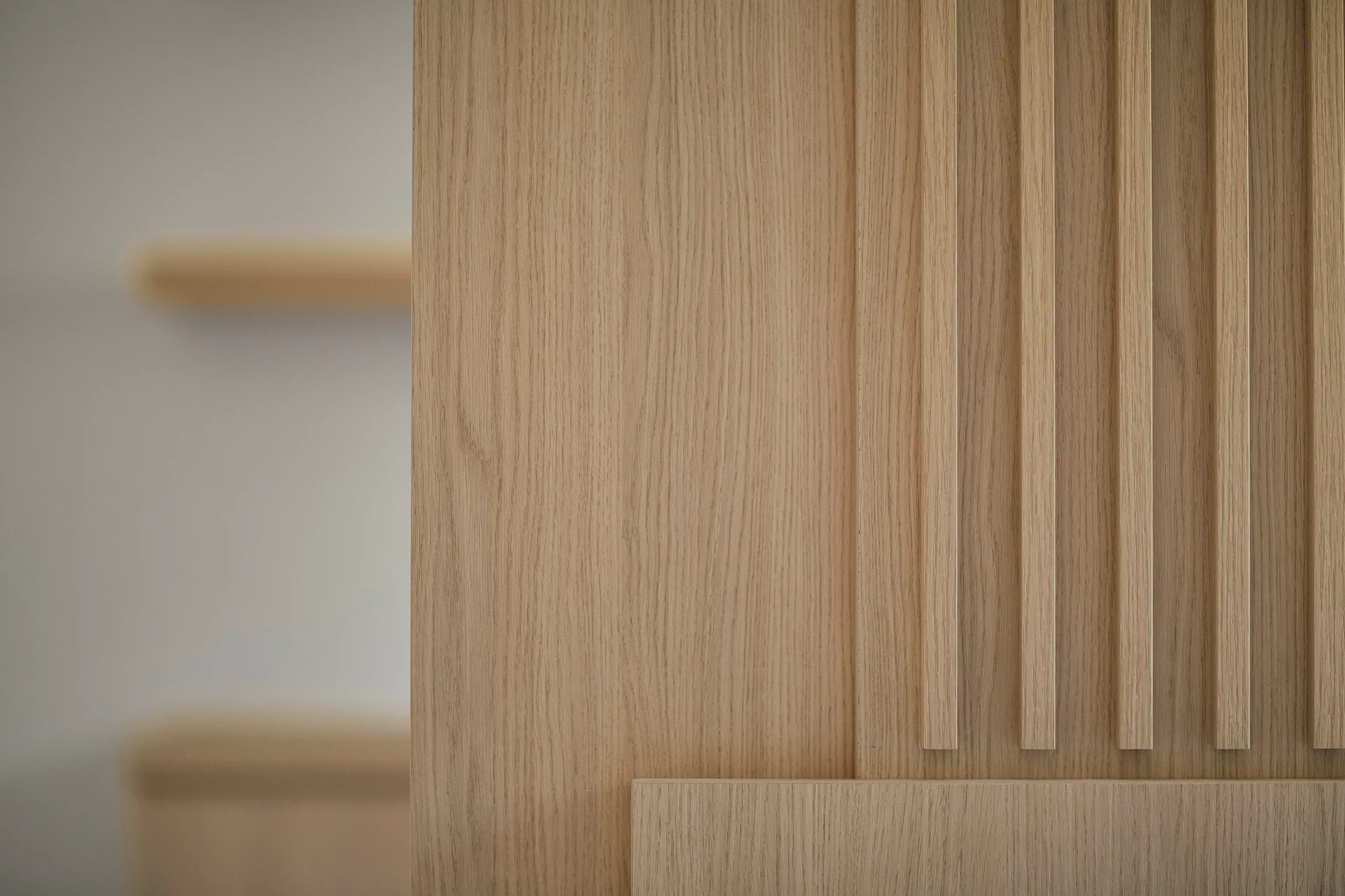 Close-up of light beige wood wall paneling featuring vertical slats and natural grain with a blurred shelf in the background.