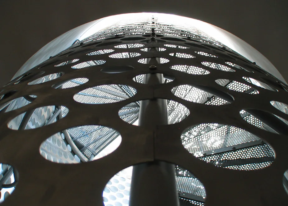 A low-angle view looking up a dark matte metal spiral staircase wrapped in a guardrail with large circular perforated cutouts.