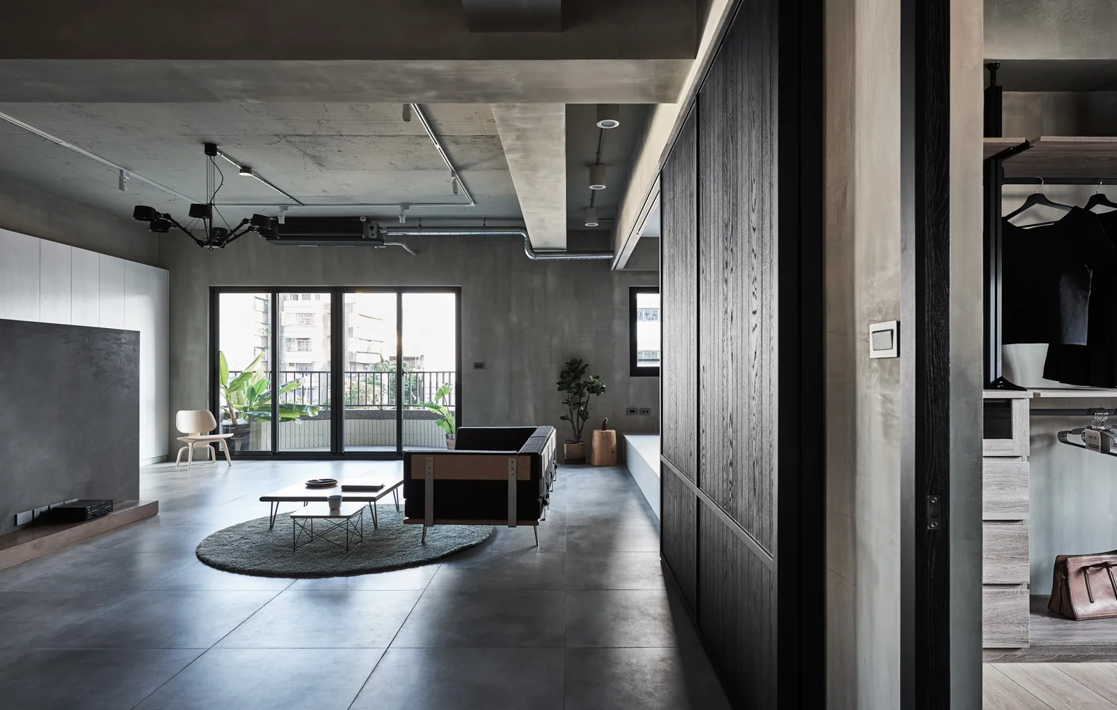 An industrial apartment living room features exposed concrete walls, a dark grey sofa on a round rug, and a large sliding wood partition.