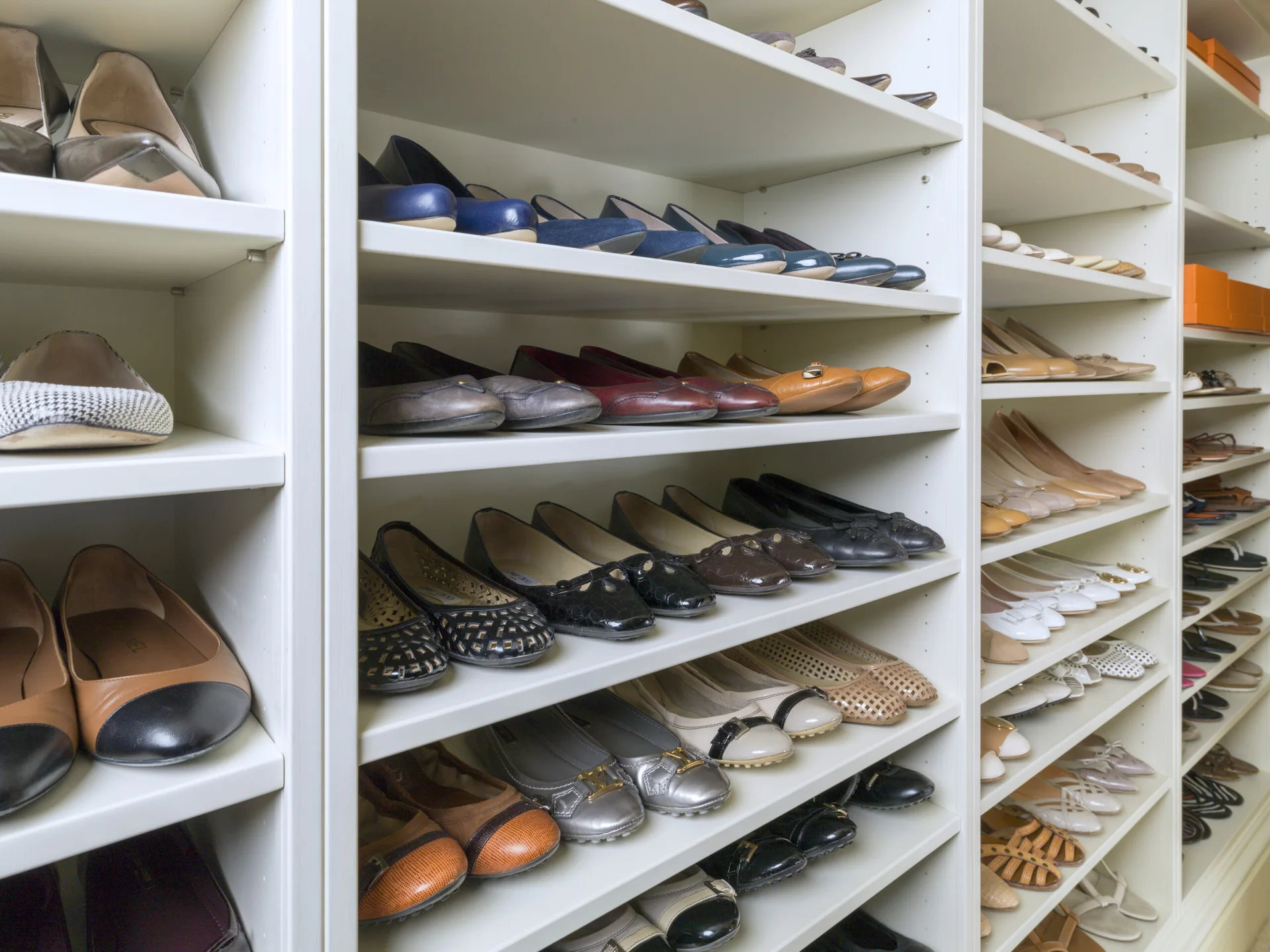 A tall white built-in closet shelving system filled with organized pairs of women's flat shoes and pumps.