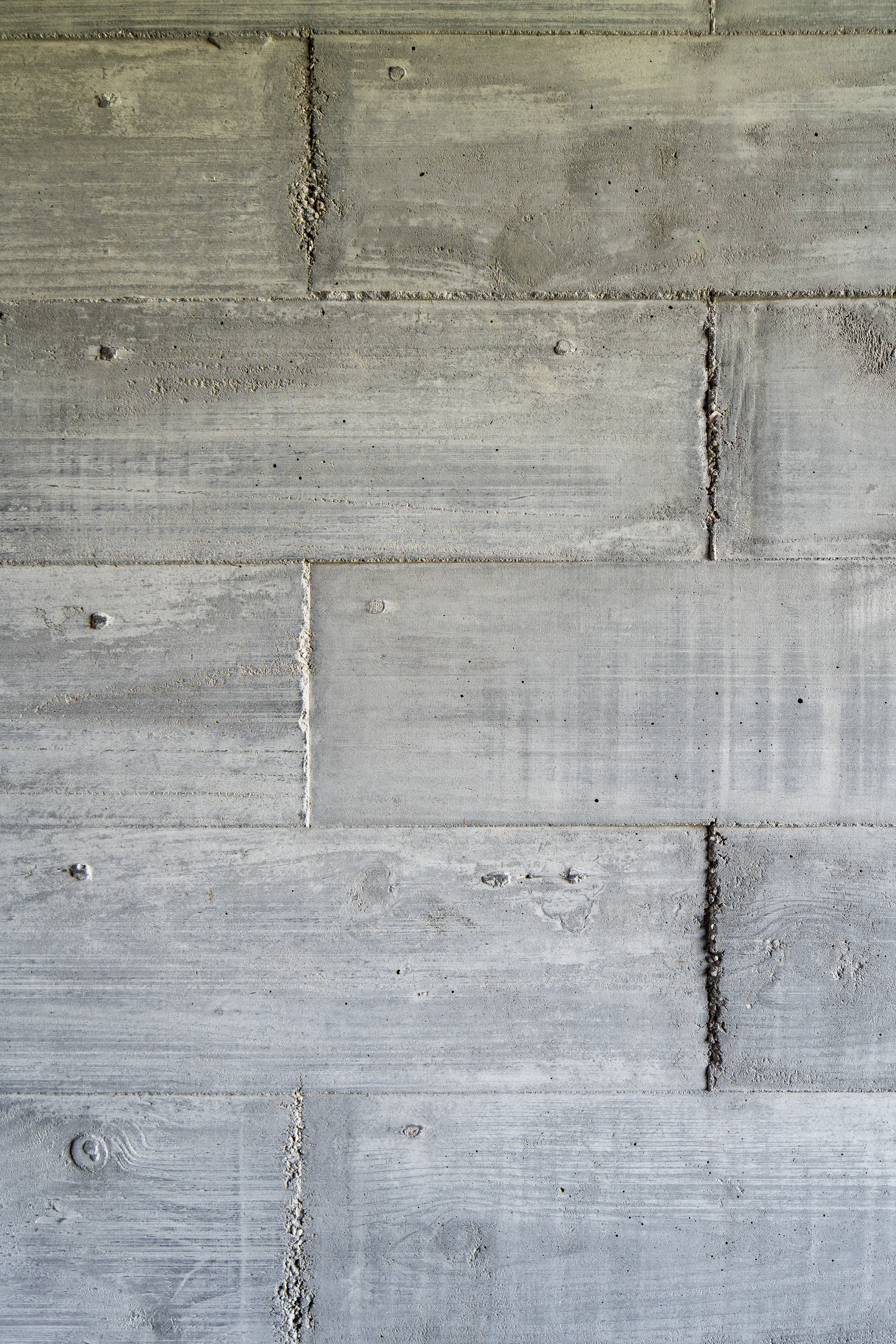 A close-up shot of a gray board-formed concrete wall showing horizontal wood grain textures, seams, and natural surface imperfections.