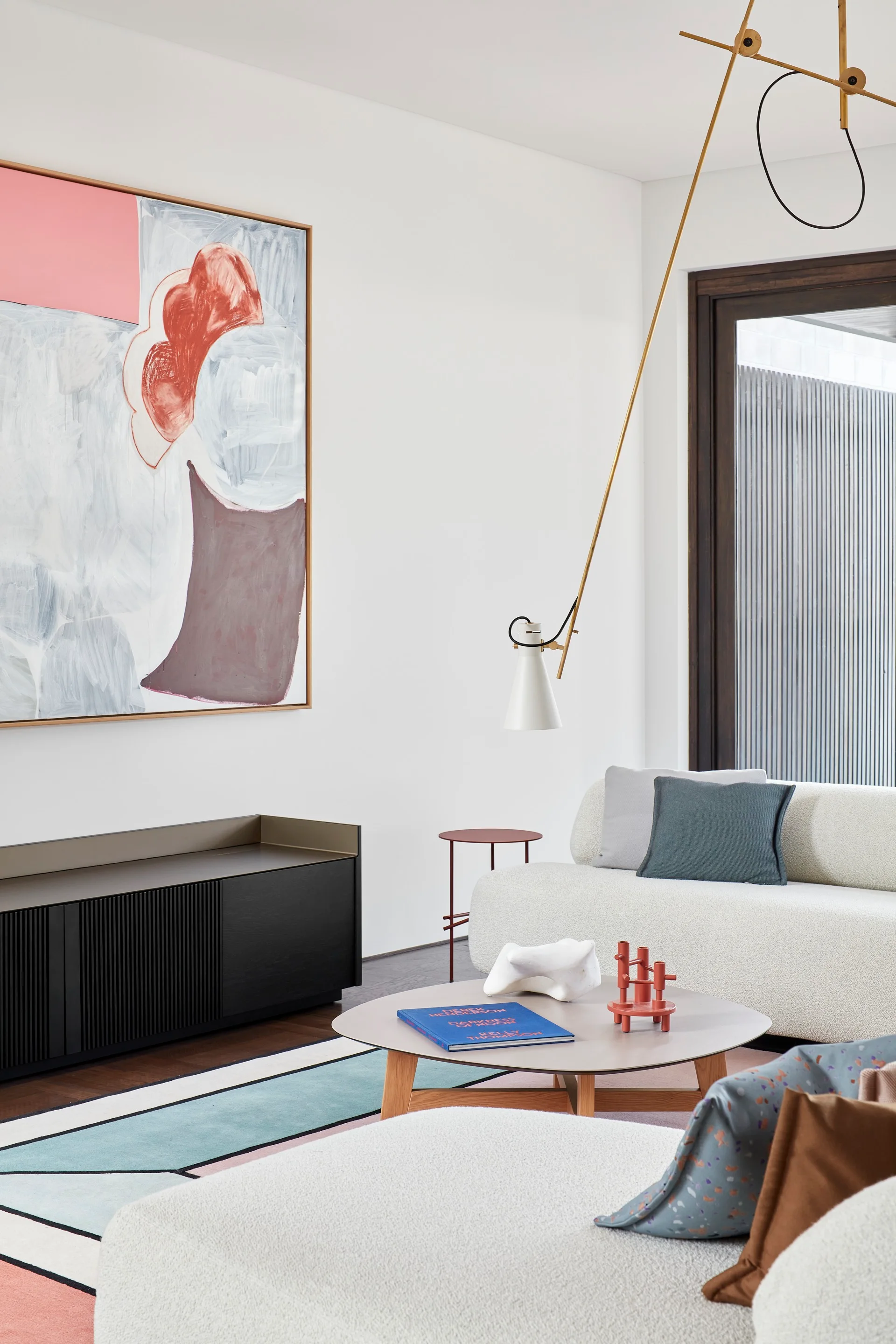 A contemporary living room with a cream textured sofa, a round coffee table, a black ribbed sideboard, and a large abstract painting.