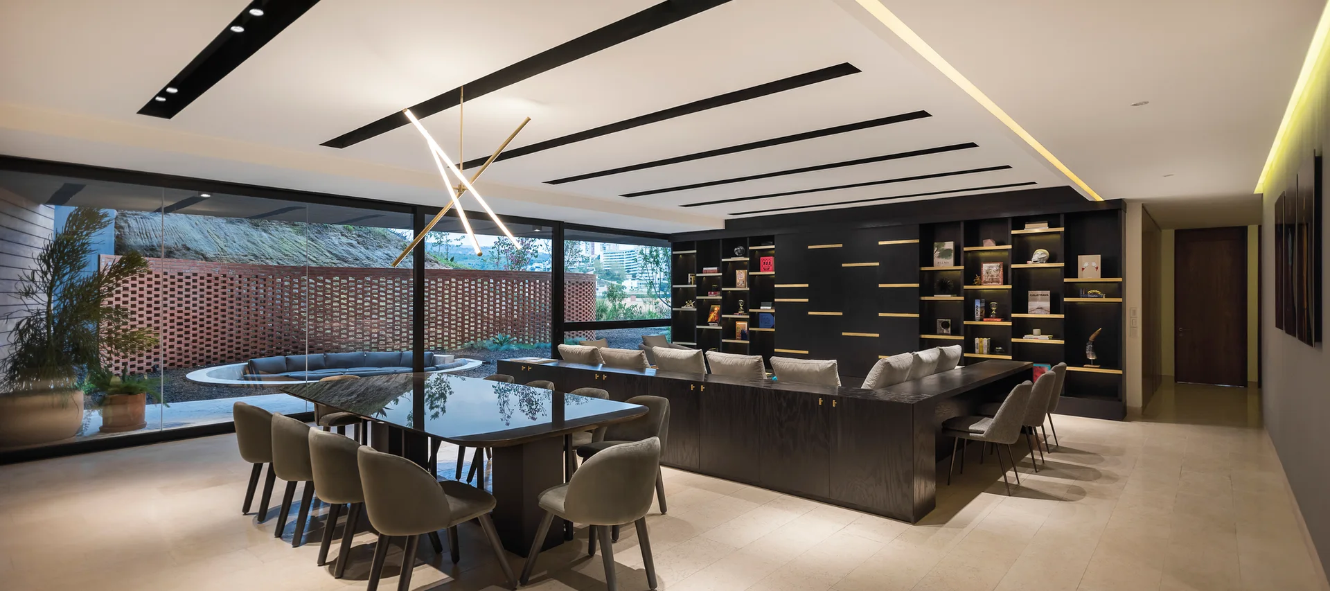 A contemporary dining room features a dark wood table, upholstered gray chairs, a black built-in shelving unit, and a glass wall showing a brick patio.