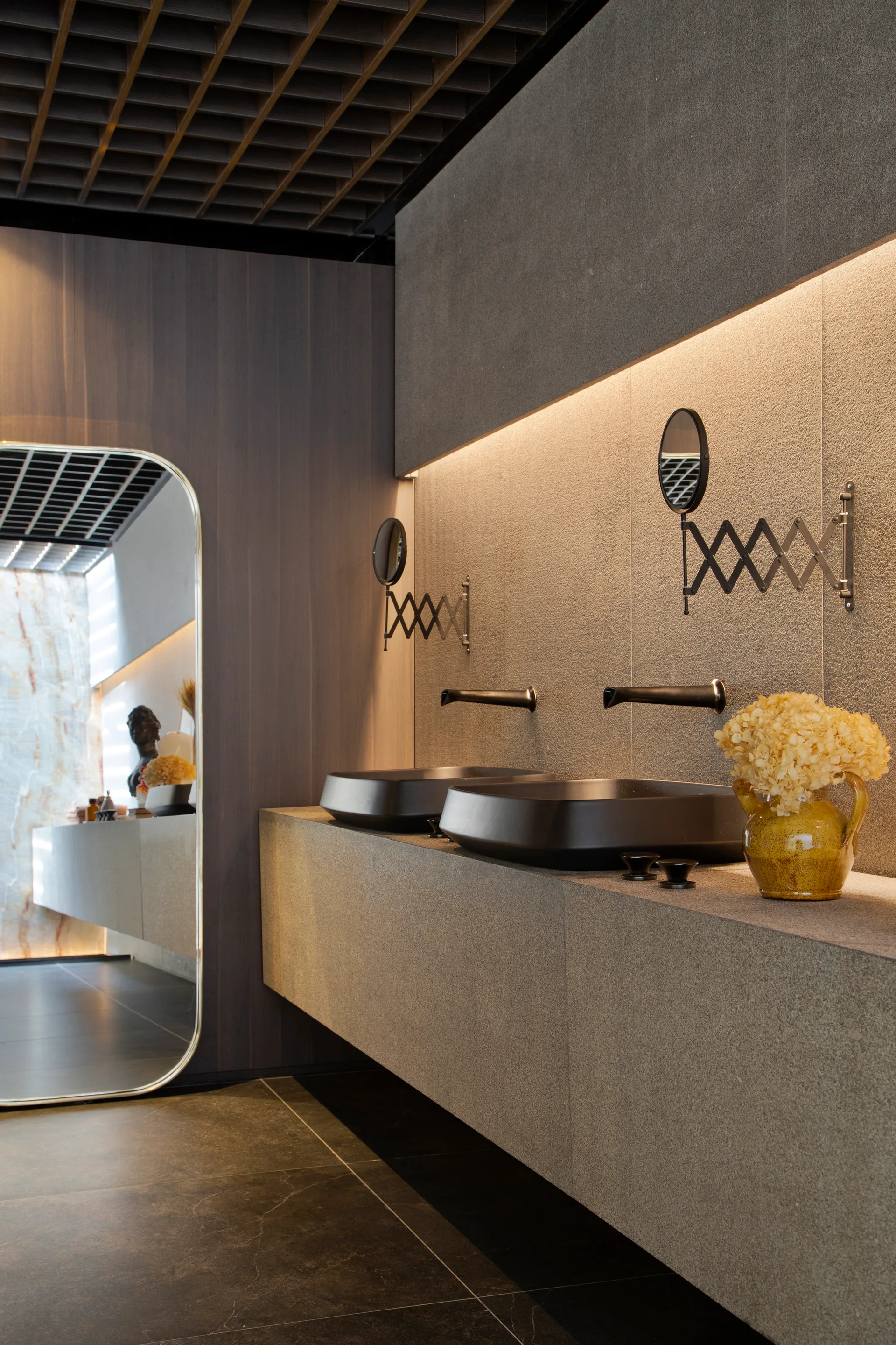 A modern bathroom vanity area features a floating stone counter with two matte black vessel sinks, wall-mounted faucets, and warm linear lighting.
