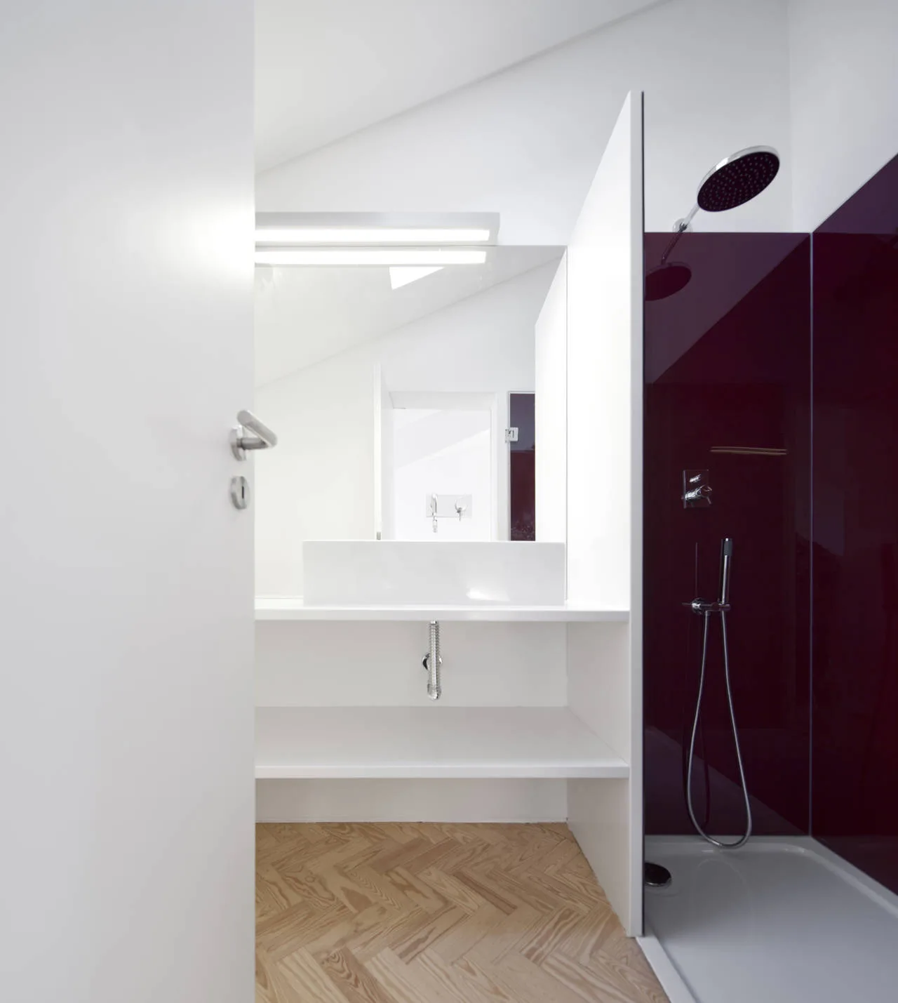 A modern minimalist bathroom featuring a white vanity, herringbone patterned wood floors, and a walk-in shower with glossy deep plum wall panels.