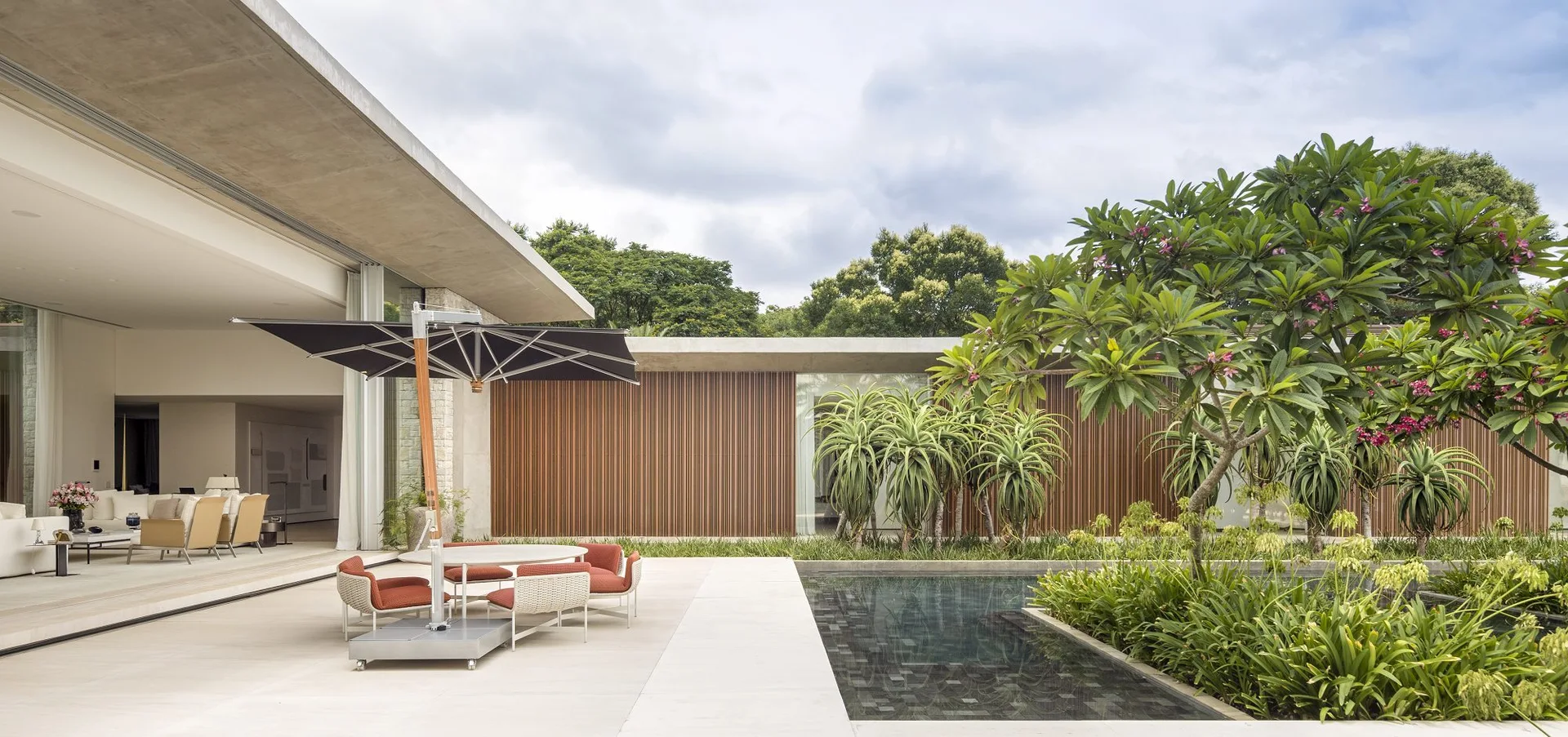 A modern outdoor patio features a black umbrella over a dining set next to a rectangular pool, flanked by a vertical slatted wood exterior wall.