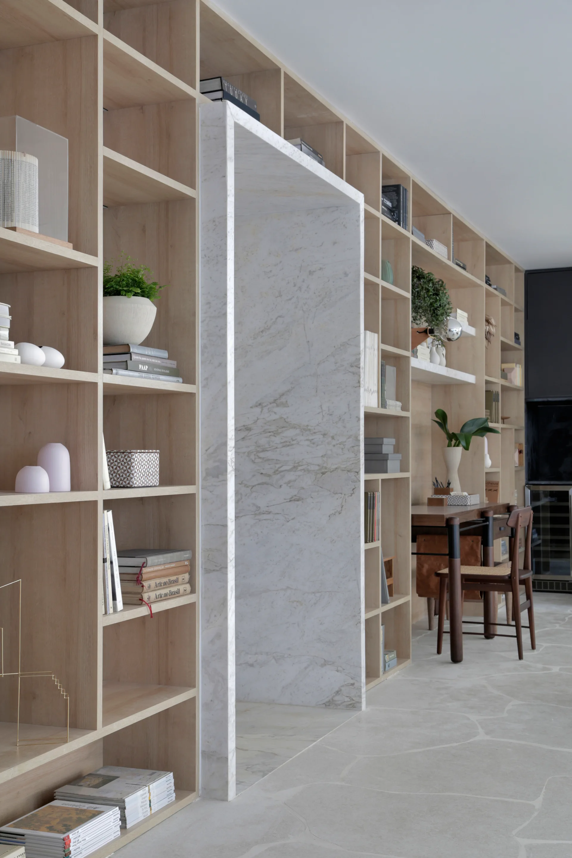 A floor-to-ceiling light wood shelving unit features an integrated white veined marble archway over flagstone flooring.