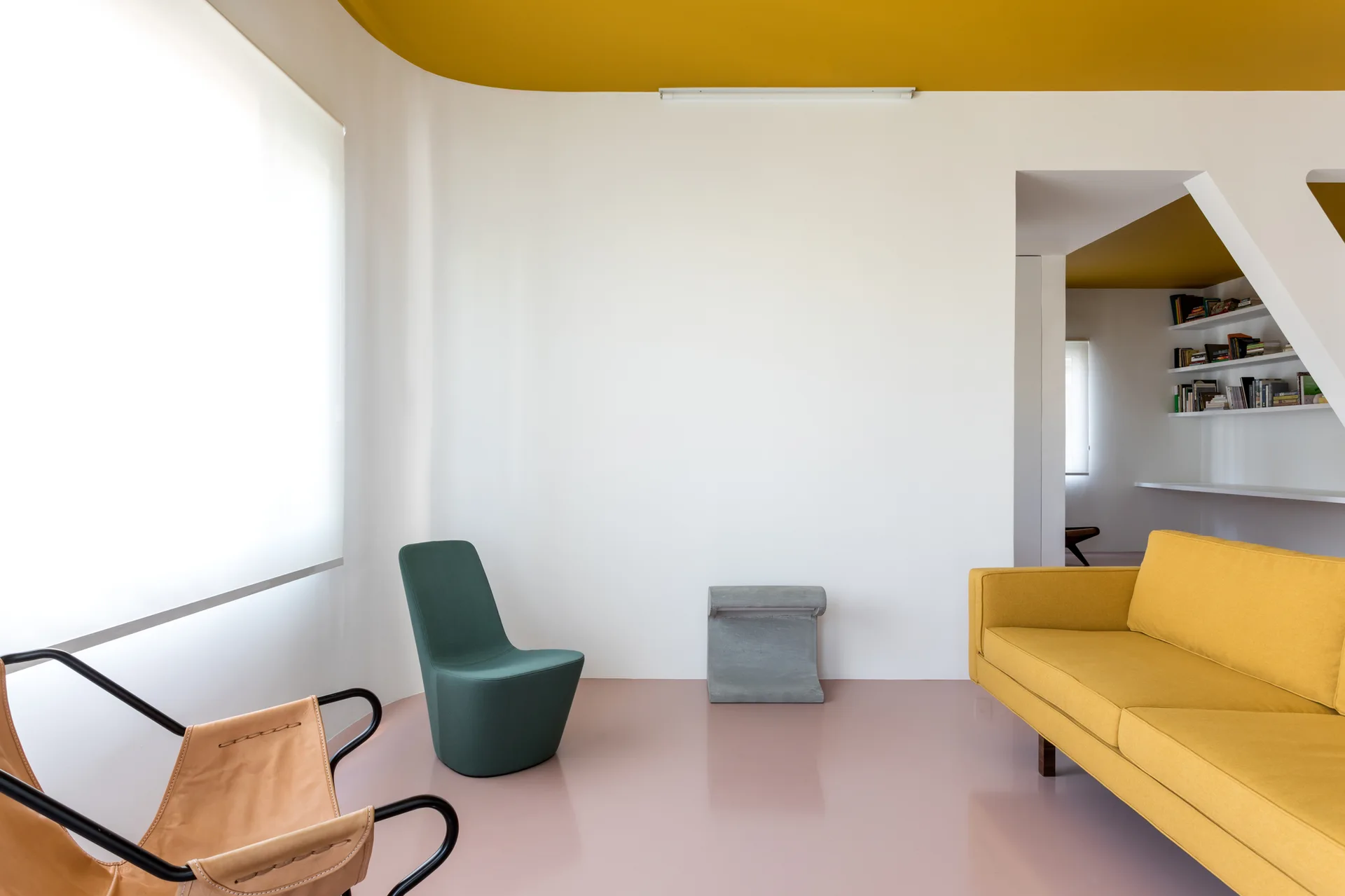 A minimalist living room features white walls, a bold yellow ceiling, a pale pink floor, a yellow sofa, and a sculptural green armchair.