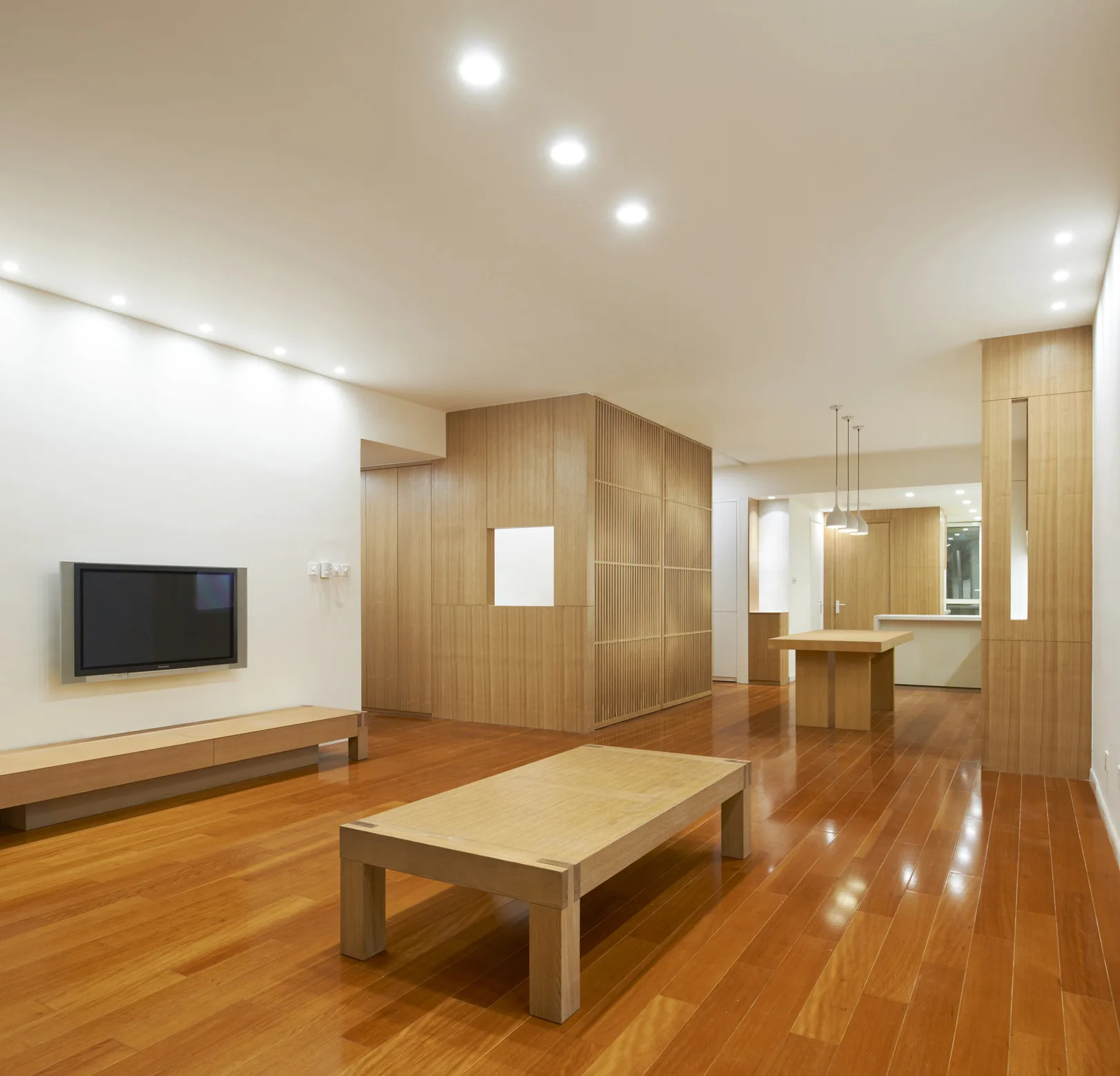 A minimalist living room features warm polished wood floors, a low-profile coffee table, and a central slatted wood room divider partition.
