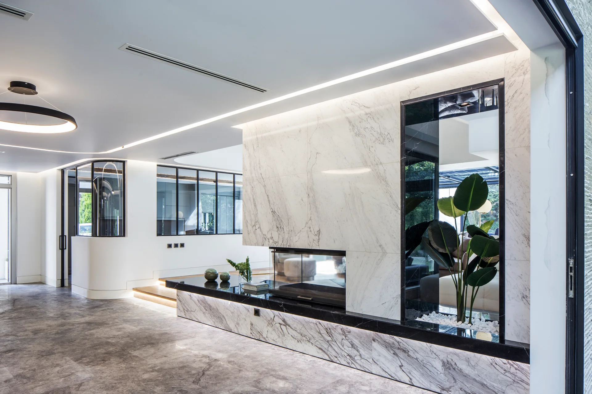 A modern living space features a large white veined marble fireplace, integrated linear ceiling lights, and grey tile floors.