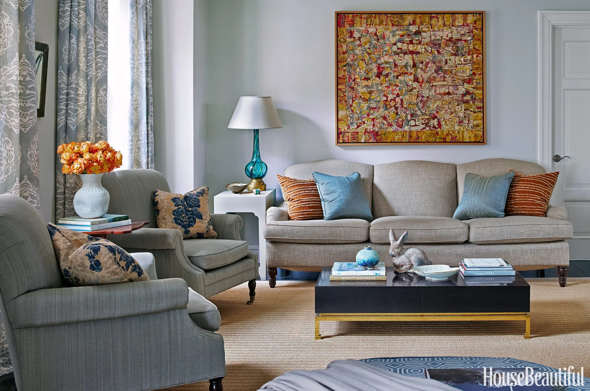 A transitional living room featuring a neutral sofa and grey armchairs arranged around a dark coffee table beneath a large abstract painting.