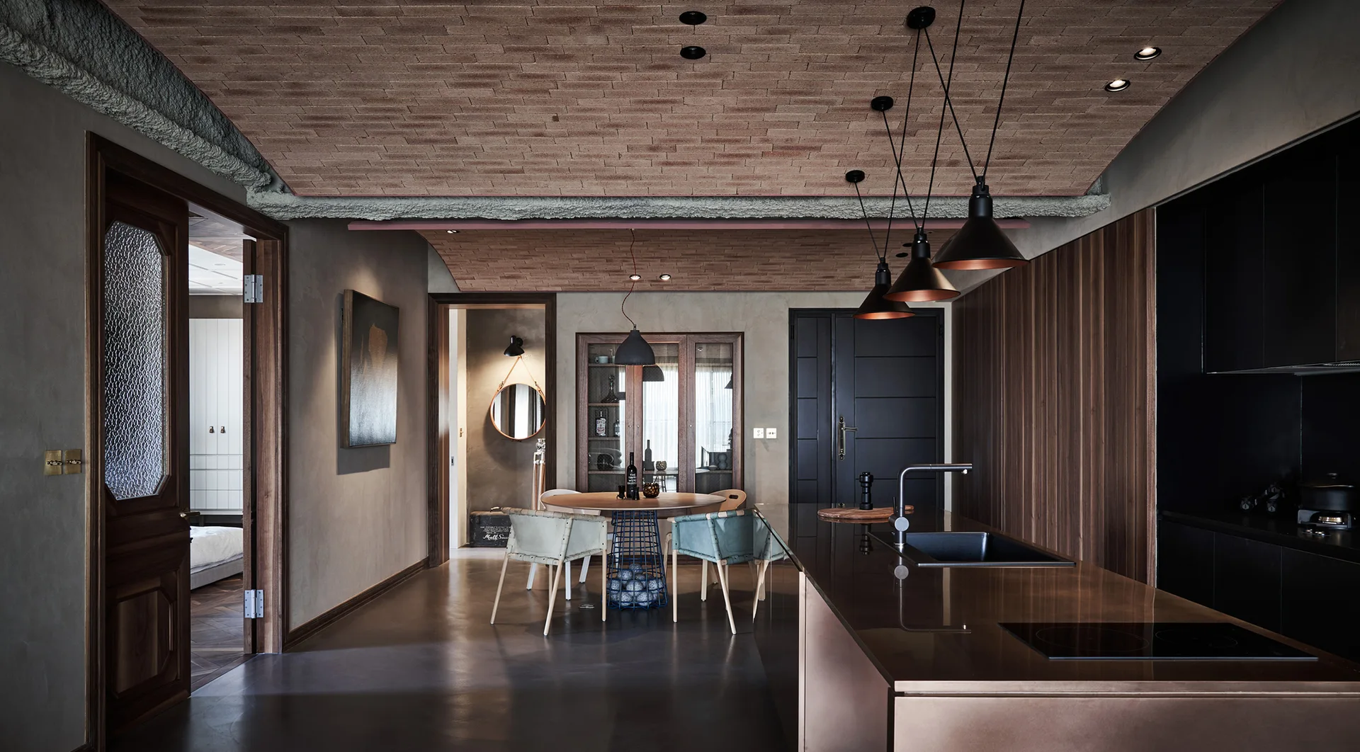 An industrial-style kitchen features a vaulted brick ceiling, a metallic kitchen island with a black sink, and a modern circular dining set.
