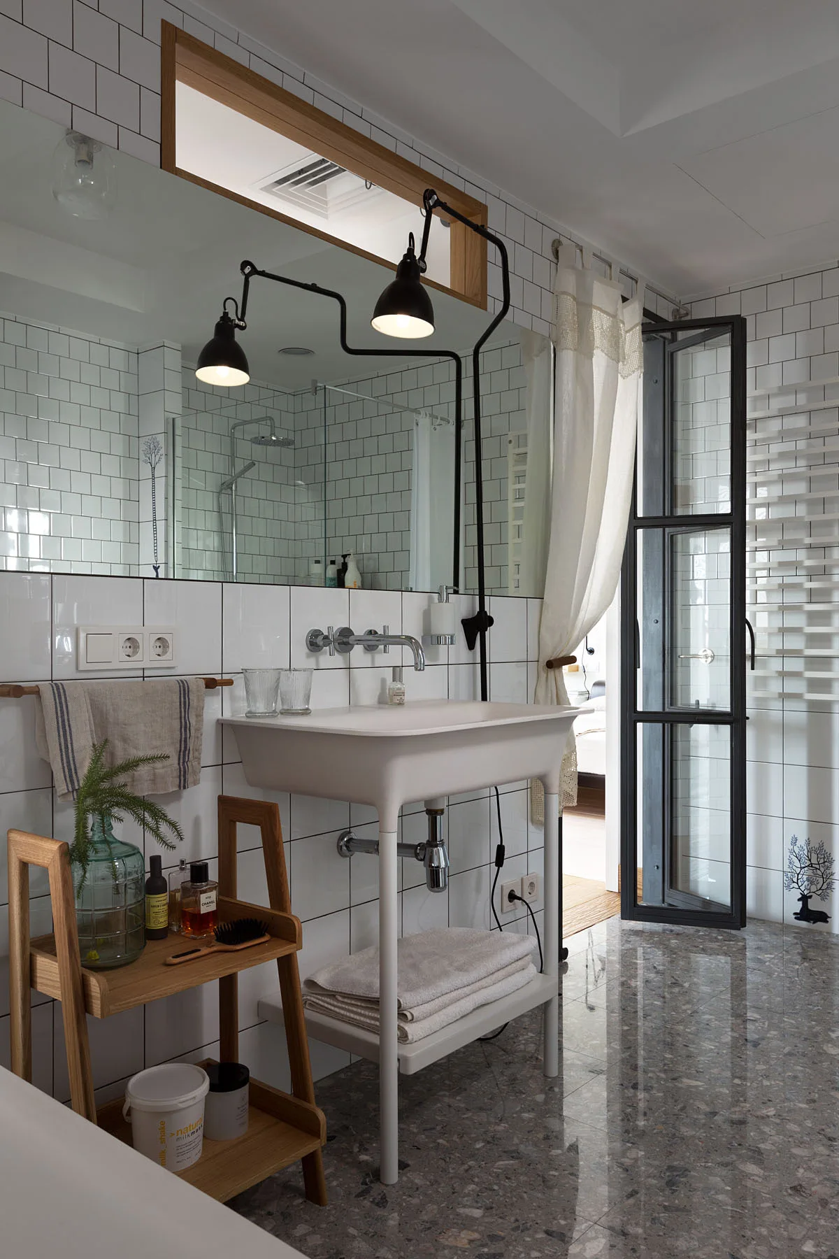 A modern bathroom features a white console sink, glossy subway tile walls, a black swing-arm lamp, and speckled grey terrazzo flooring.