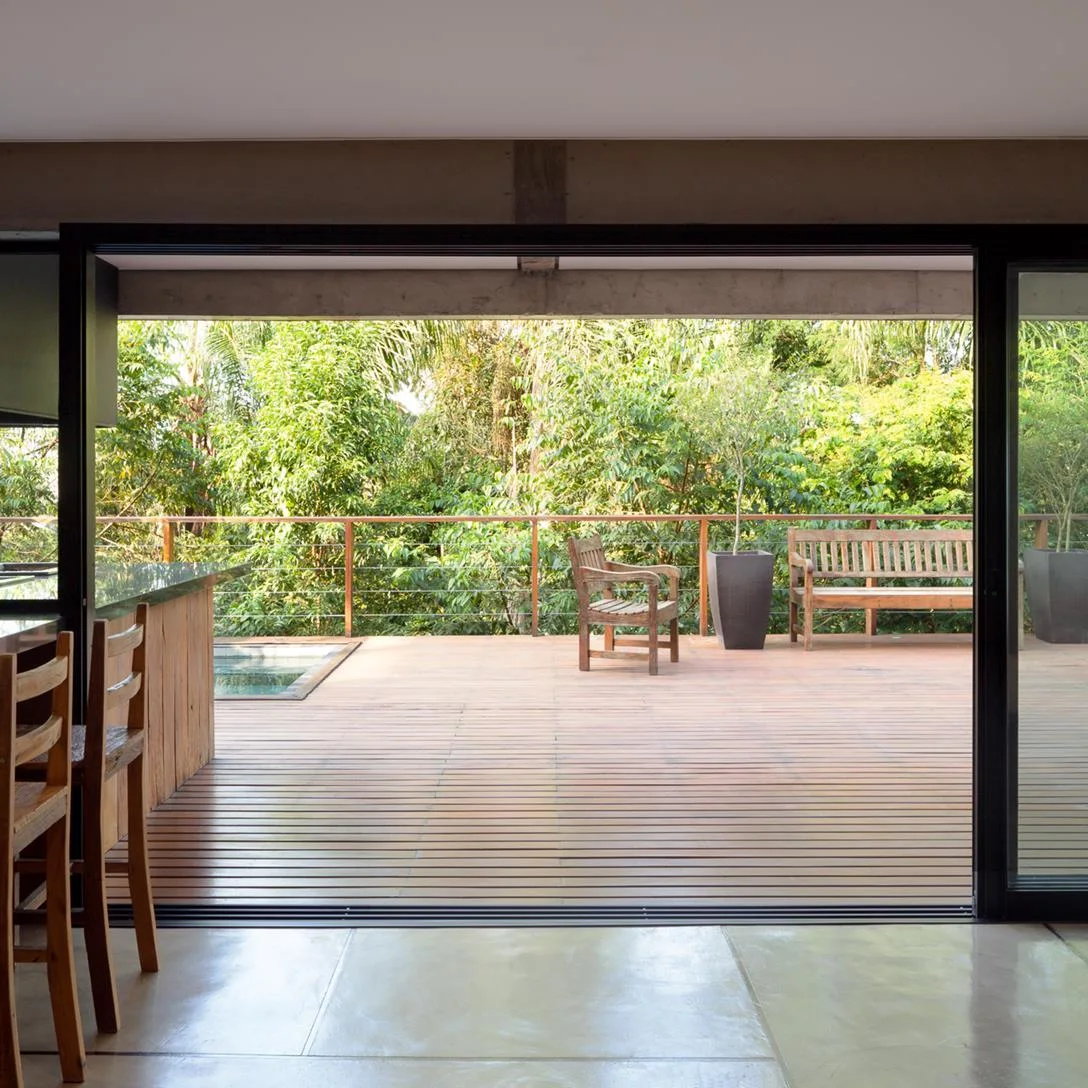 A view from polished concrete floors looking through open sliding doors onto a wooden deck with outdoor furniture, potted plants, and a pool.