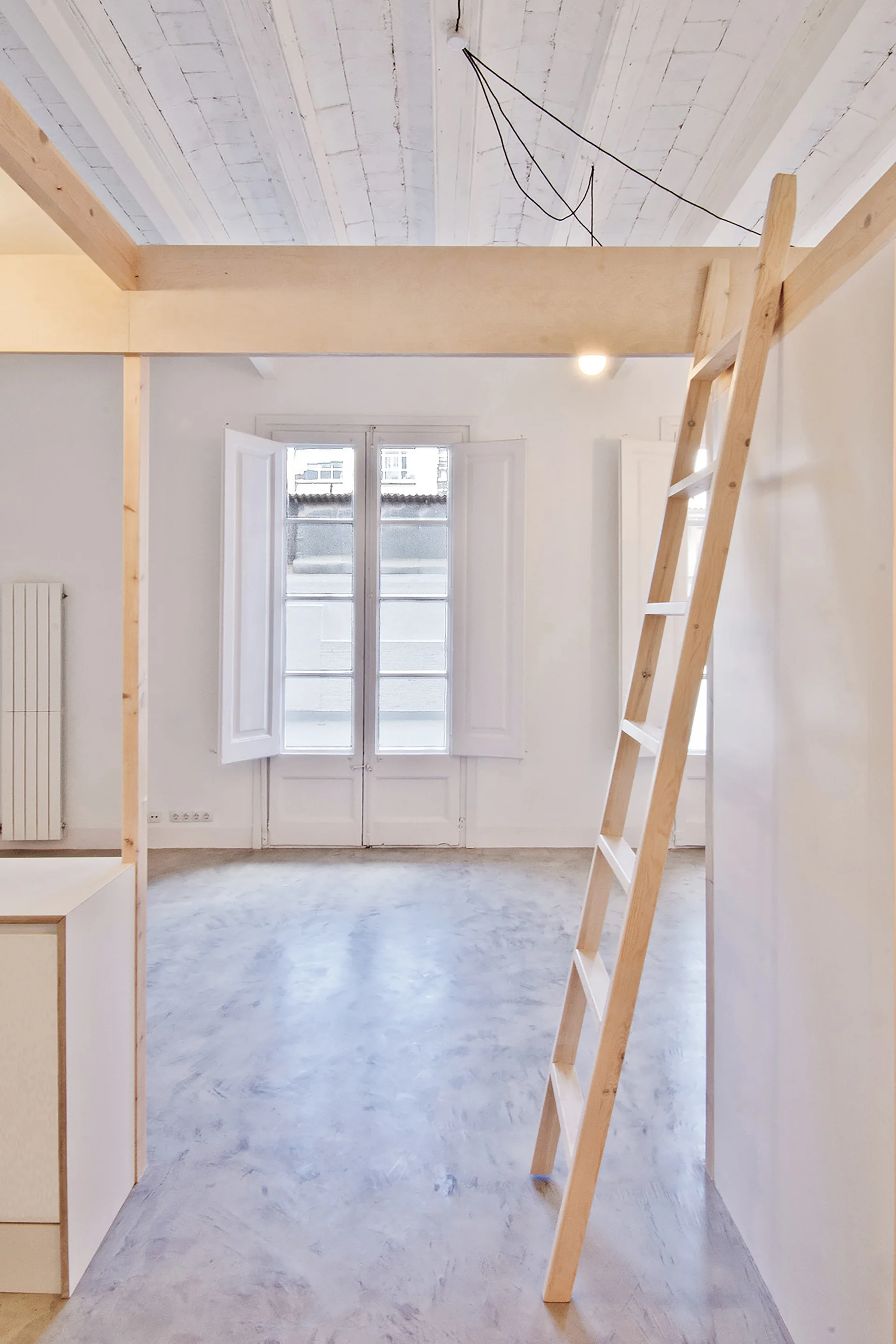 A minimalist room featuring a light wood structural frame with a leaning ladder, polished concrete floors, and white shuttered windows.