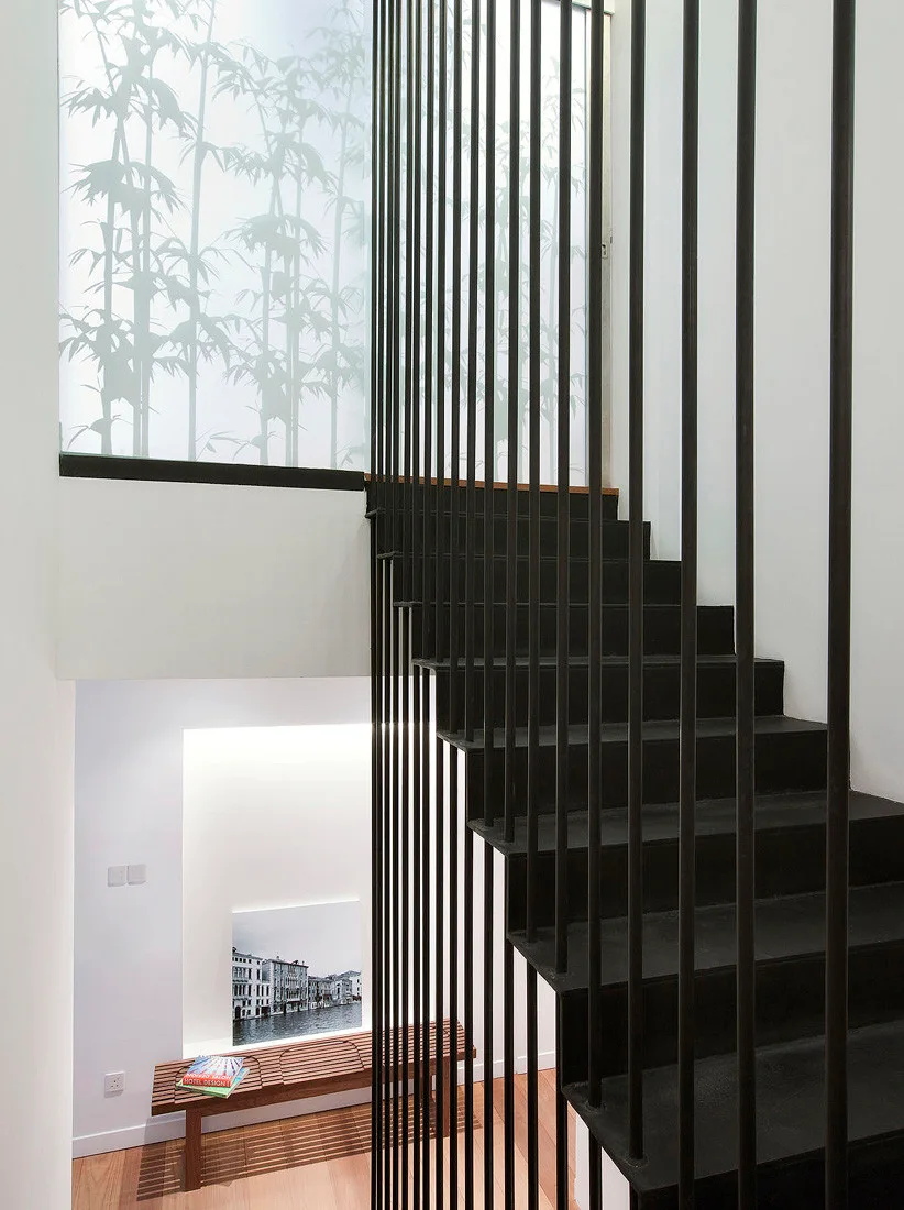 A minimalist black metal staircase with floor-to-ceiling vertical balusters next to a wooden slatted bench.