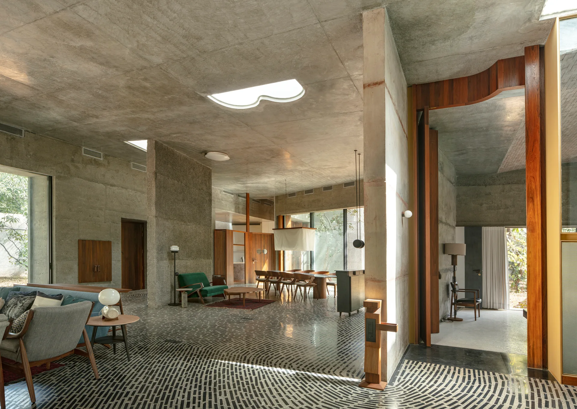 A spacious open-plan concrete living room features patterned mosaic tile flooring, mid-century modern furniture, and an organic-shaped ceiling skylight.