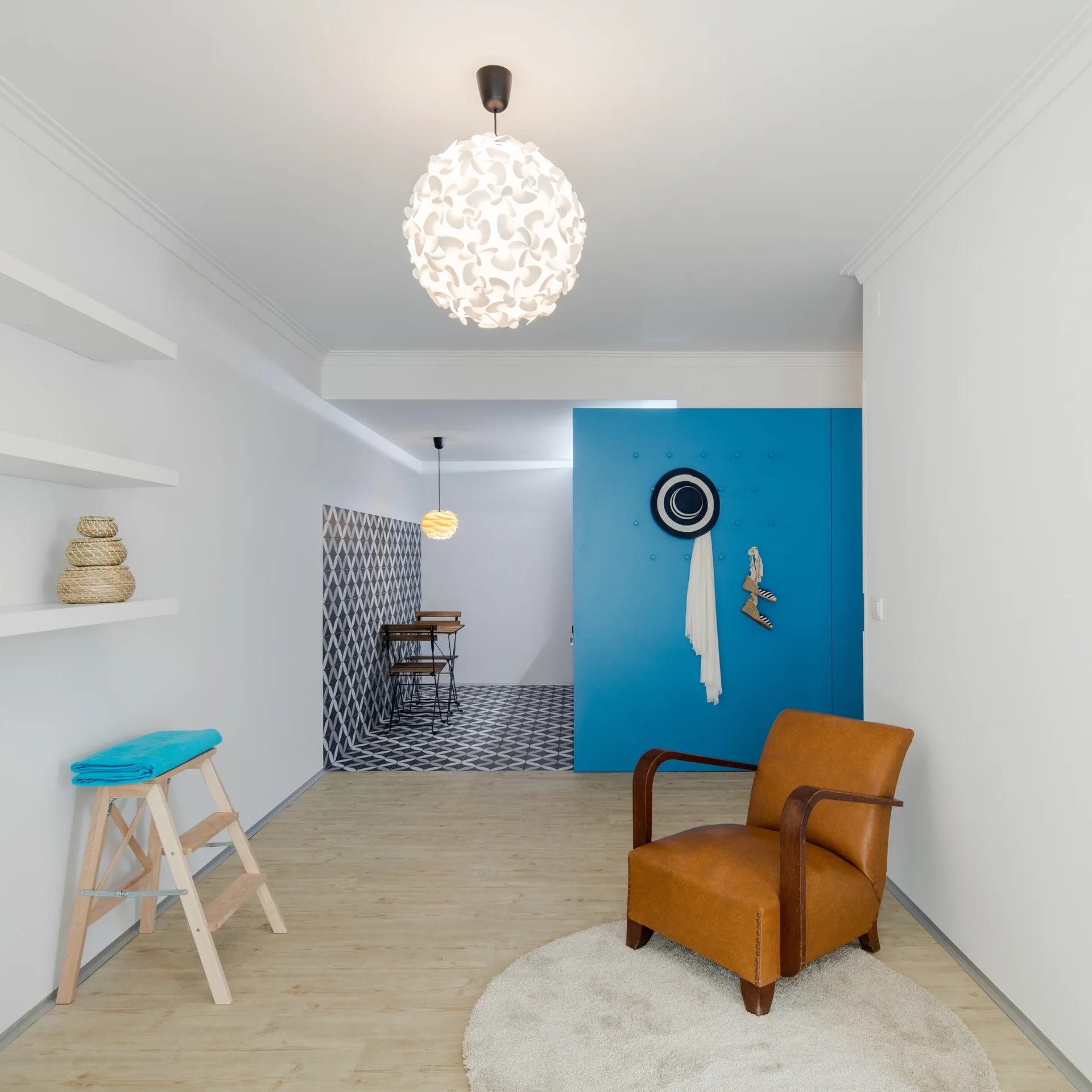 A tan leather armchair sits on a round cream rug in a bright room with a vibrant blue partition wall and patterned floor tiles in the background.