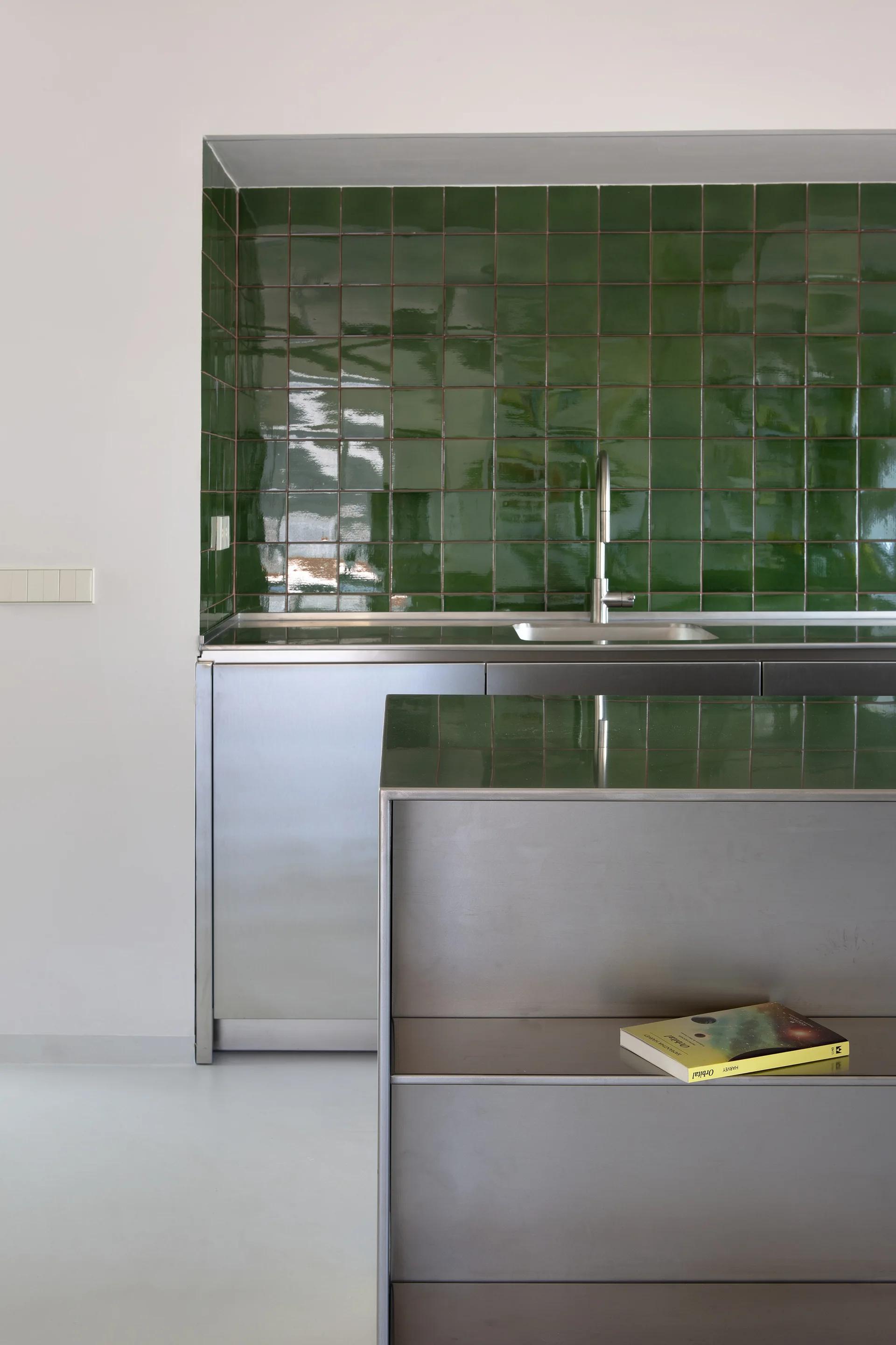 A minimalist kitchen featuring brushed stainless steel cabinets, an integrated sink, and a glossy green tiled backsplash.