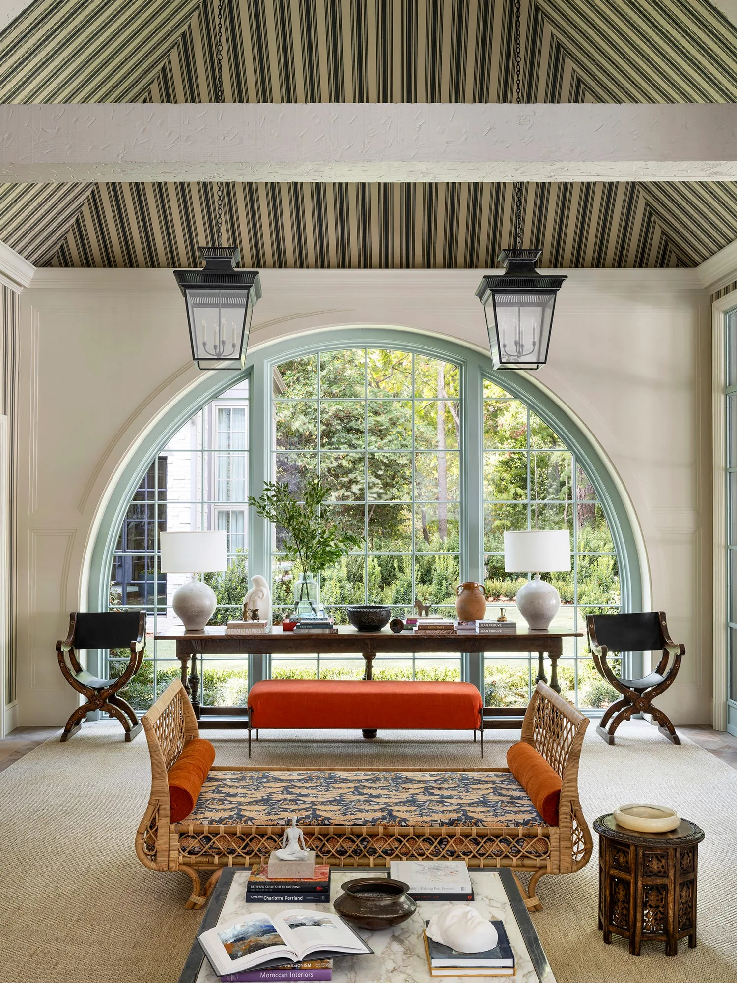 A bright living room features a wicker daybed, a green-framed arched window, and a striped vaulted ceiling.