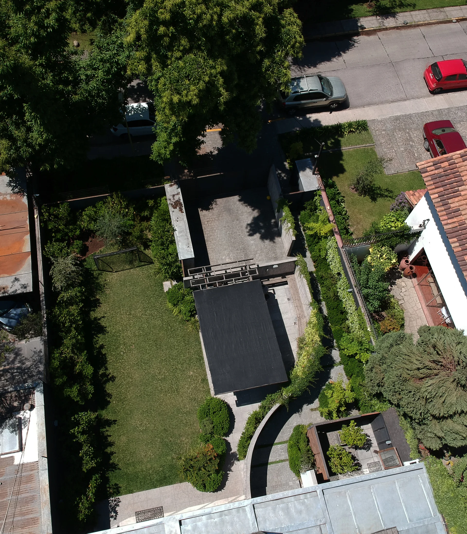 Aerial view of a landscaped backyard garden featuring a green lawn, curved stone retaining walls, paved paths, and a black covered patio.