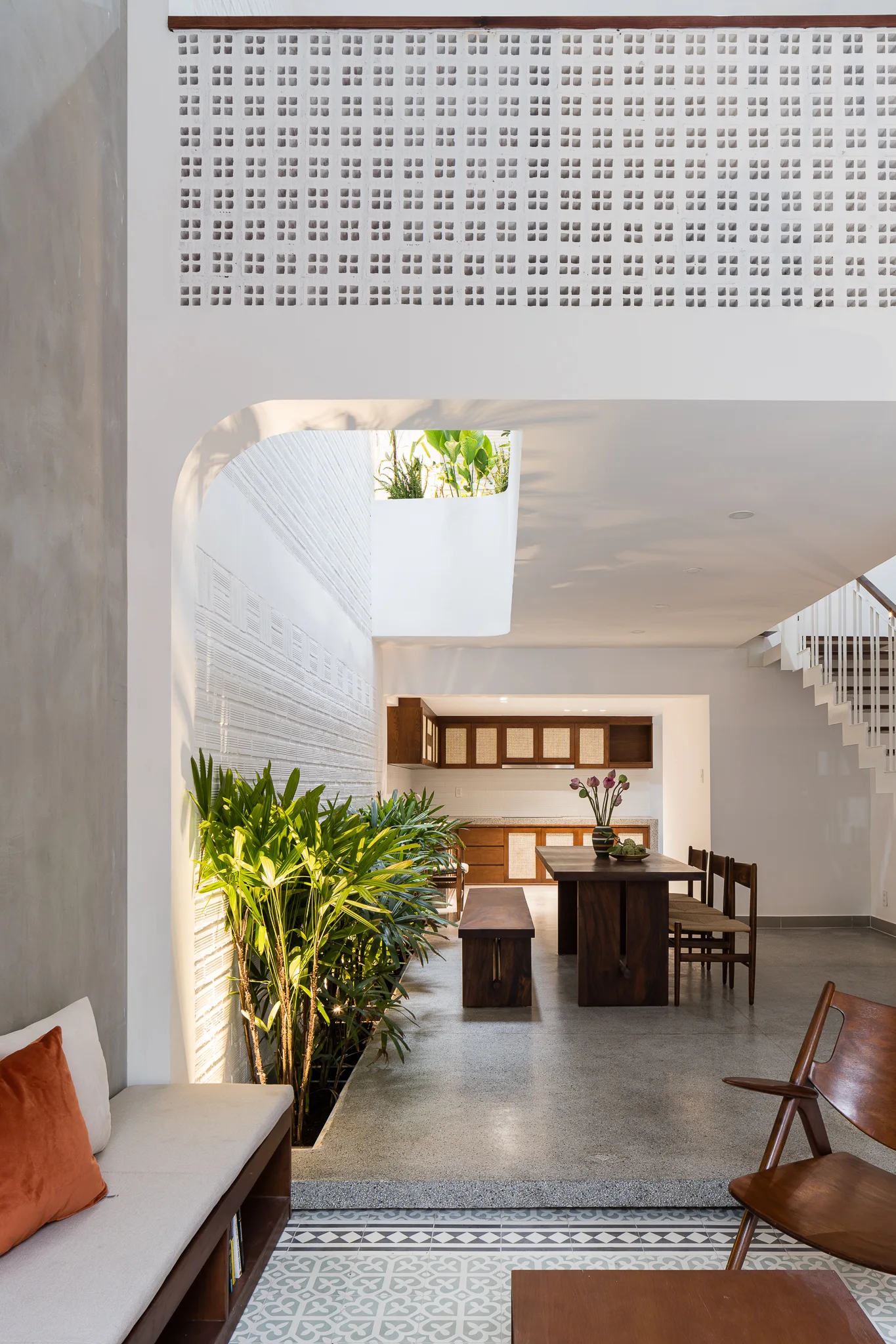 A bright modern dining room featuring a wooden table, built-in indoor garden under a skylight, and a decorative white breeze block wall.