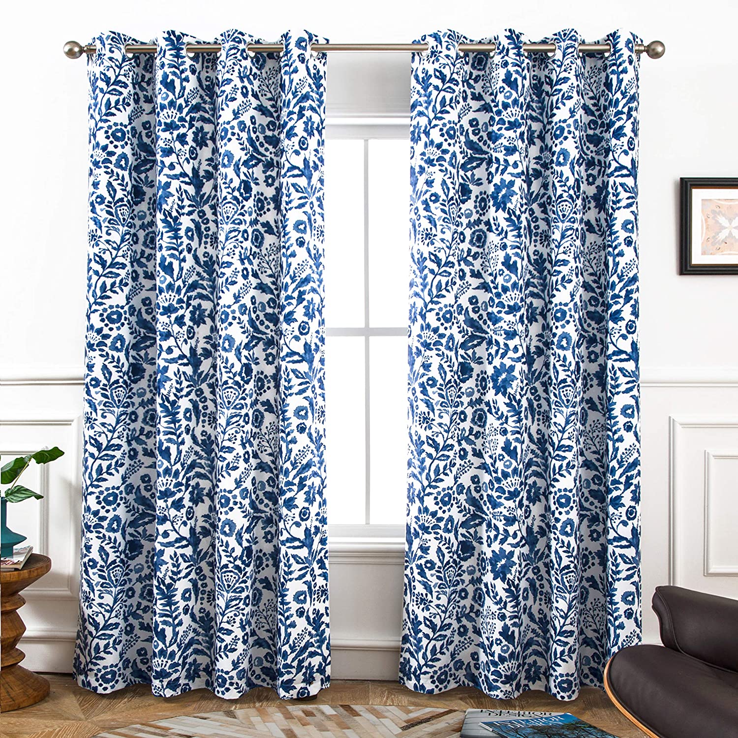 A pair of blue and white floral curtains hangs from a metal rod in front of a window in a room with white wainscoting.