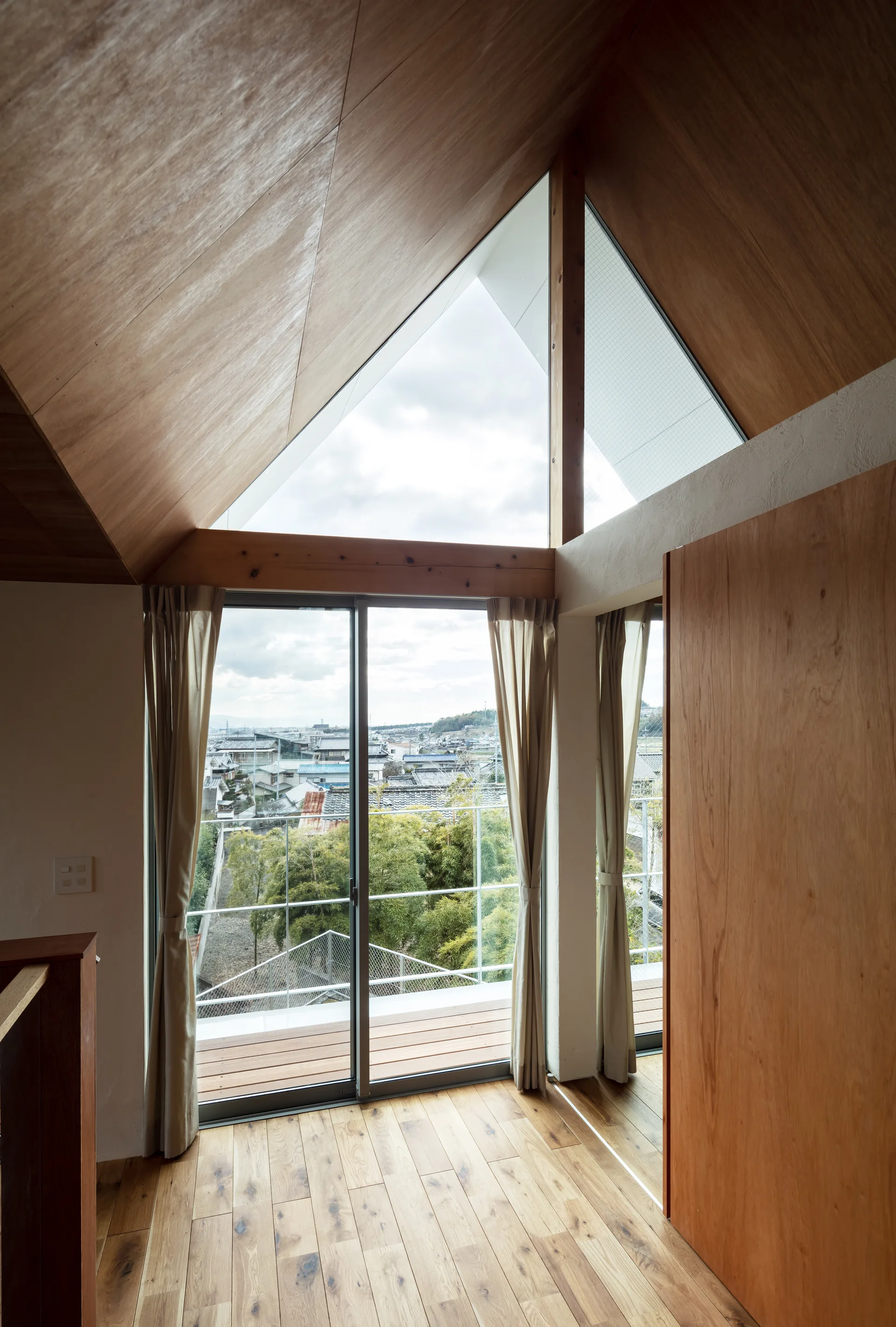 A bright loft room features a vaulted wood ceiling, a triangular top window, and sliding glass doors that open to a balcony.
