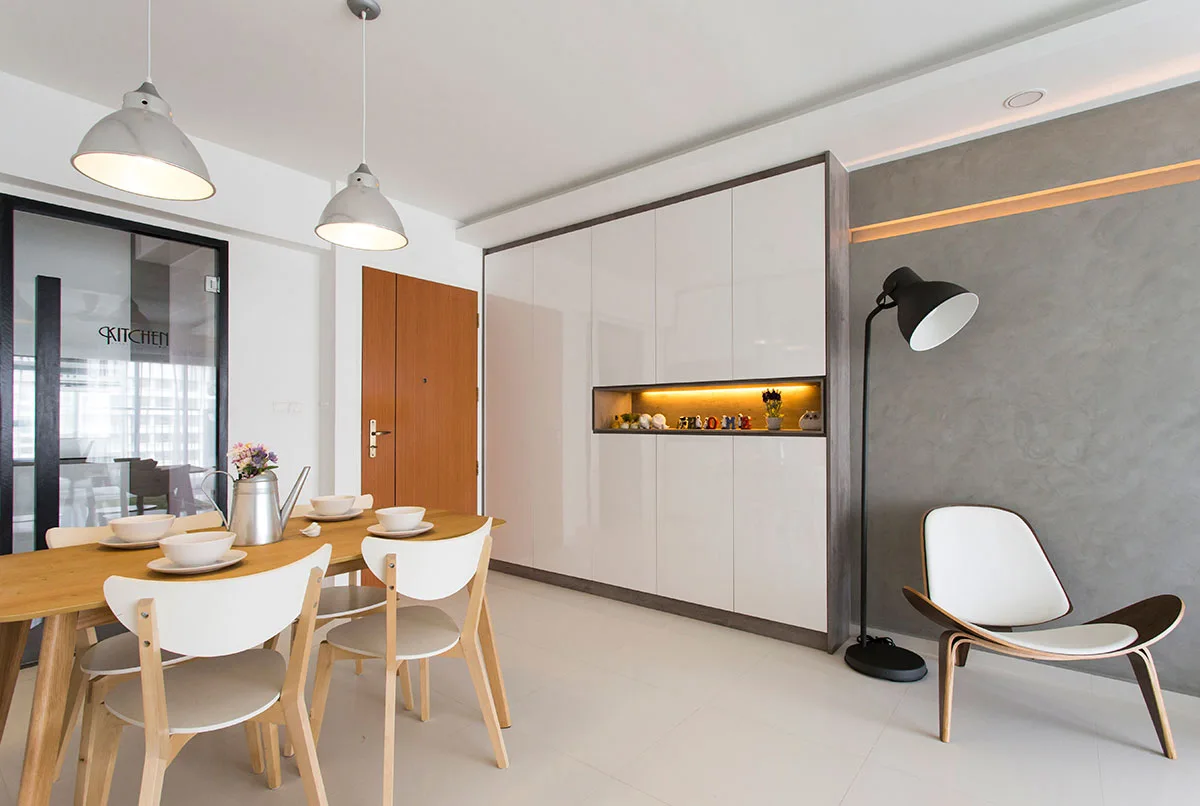 A modern dining room features a wooden table with white chairs, a large white glossy built-in cabinet with a lit niche, and a grey feature wall.