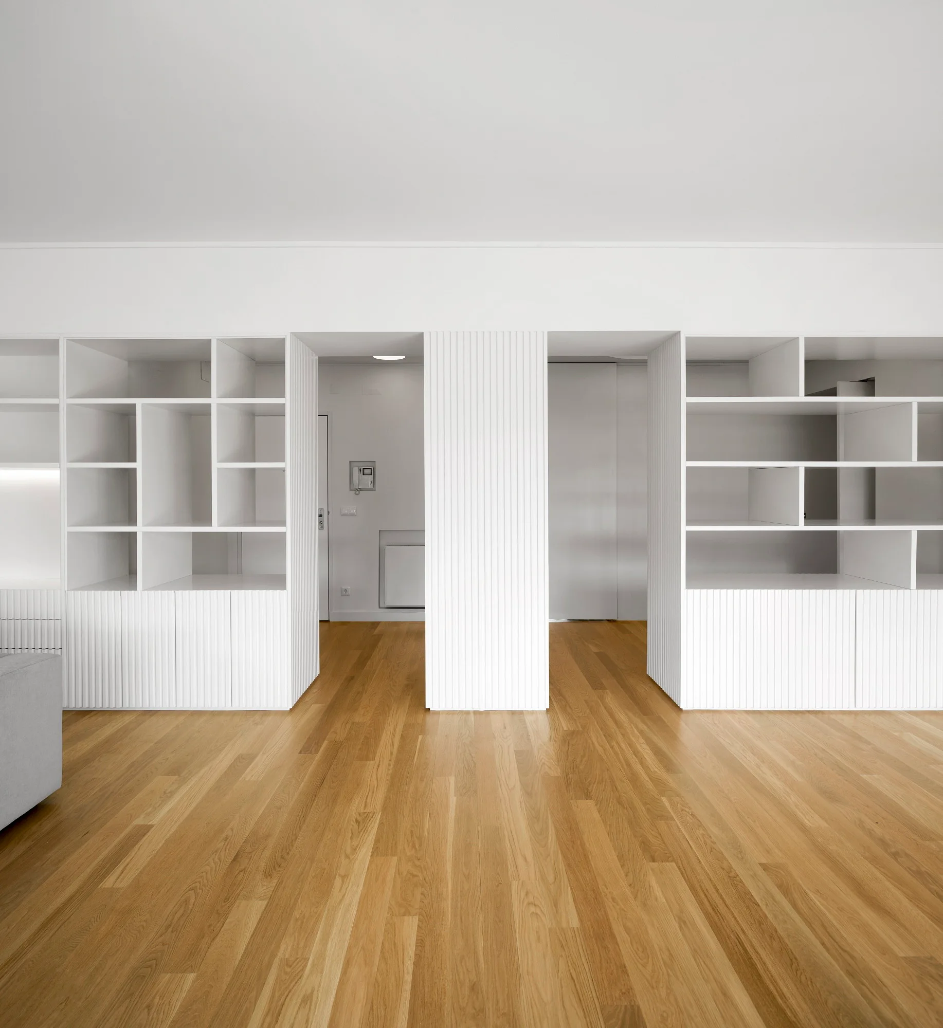 White built-in shelving units with fluted cabinet fronts frame symmetrical doorways over a light oak wood floor.