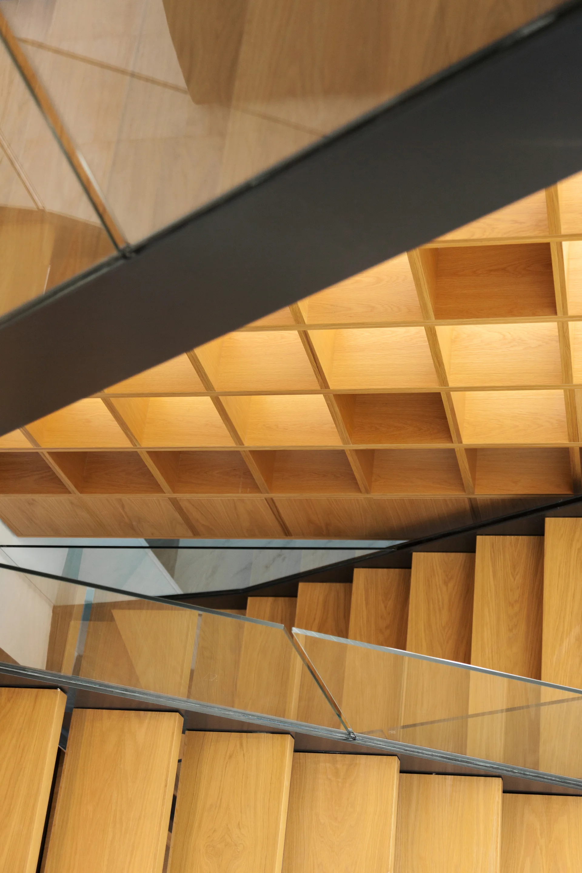 An overhead view of a light wood staircase with a glass railing and an integrated wooden grid cubby shelving system.