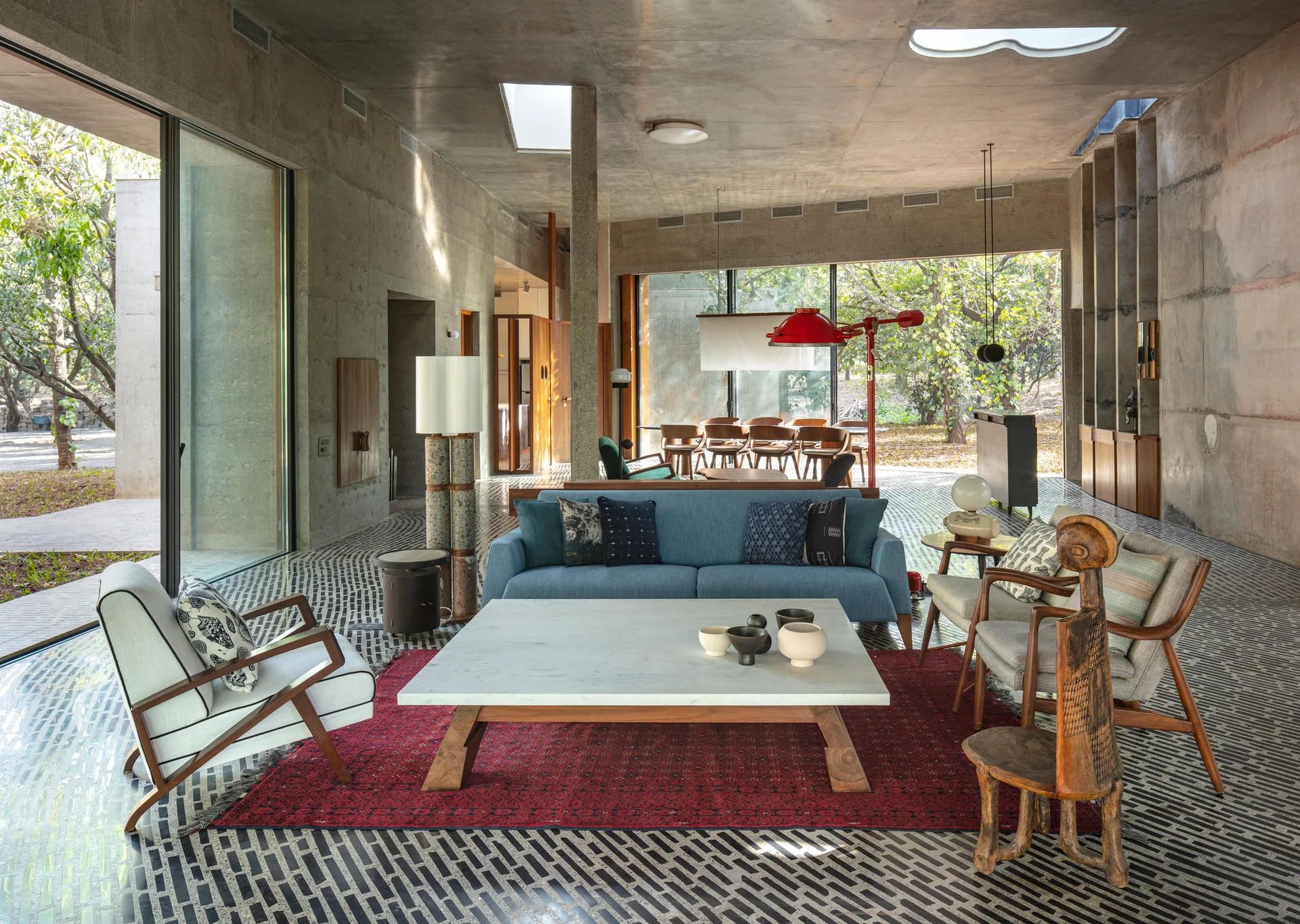 A spacious living room features exposed concrete walls, a blue sofa on a red rug, and a distinctive black and white patterned tile floor.