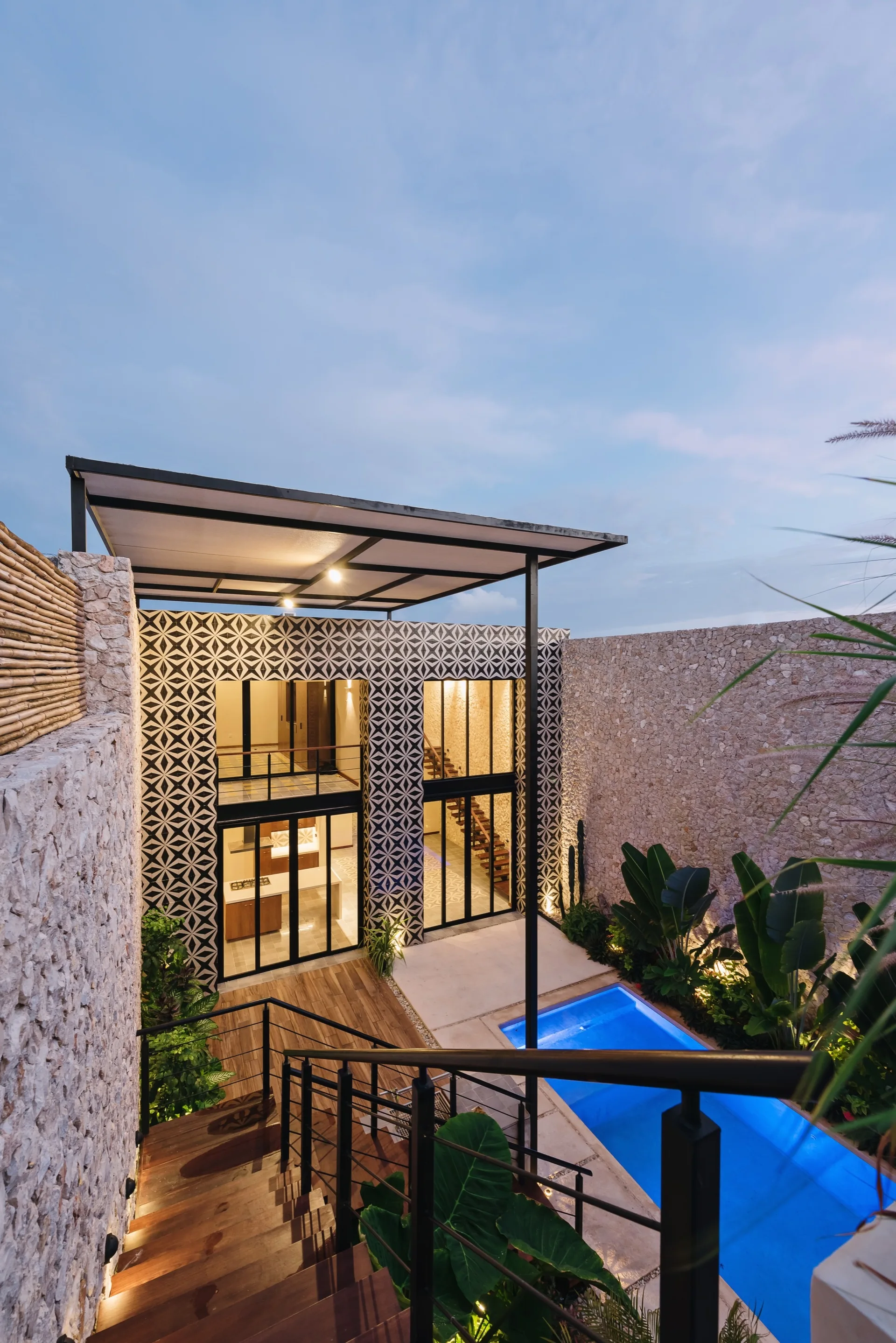 An outdoor residential courtyard features a swimming pool, wooden stairs, textured stone walls, and a facade with geometric tiles.