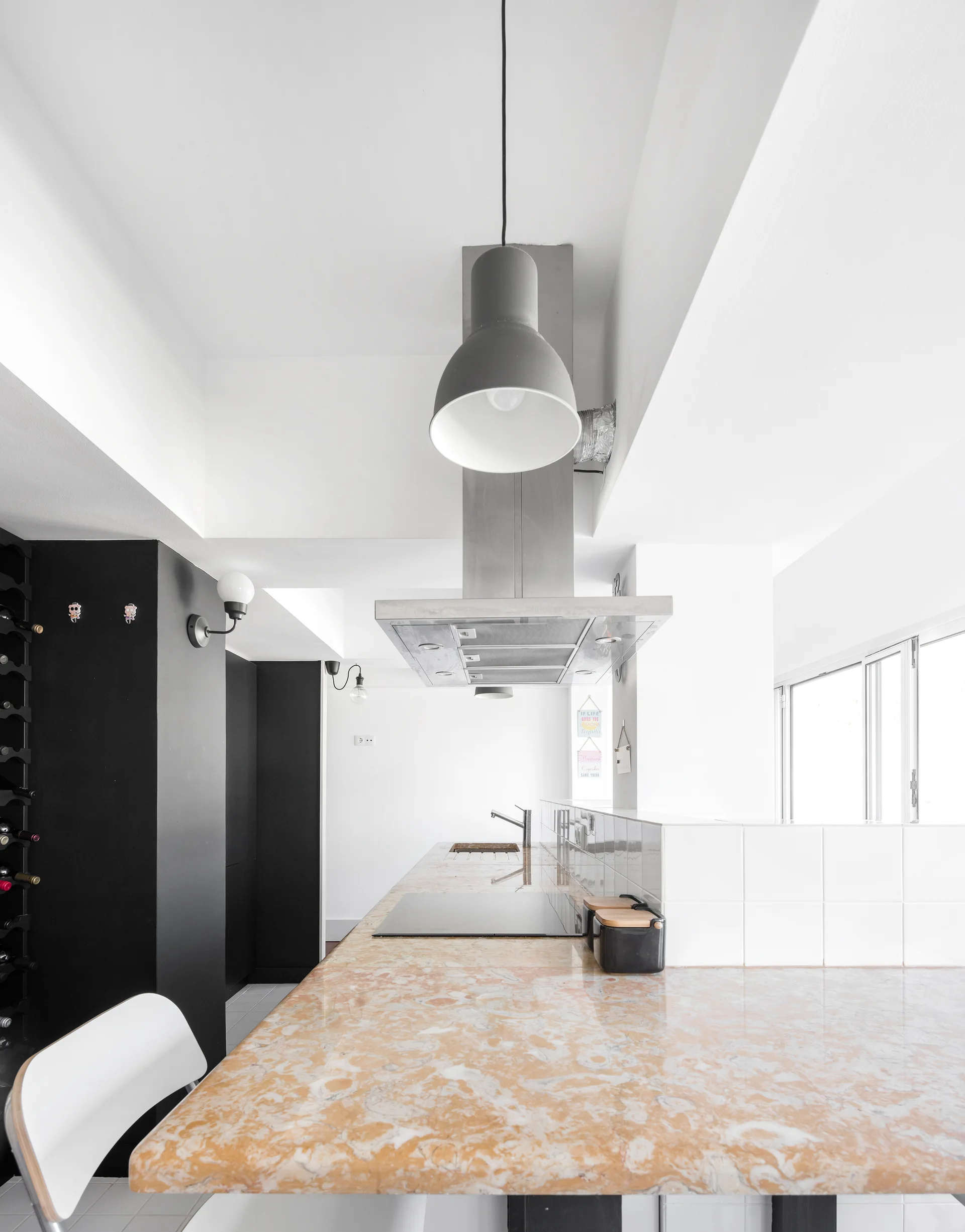 A modern kitchen features a long amber marble island with an integrated cooktop, a stainless steel range hood, and matte black cabinetry.