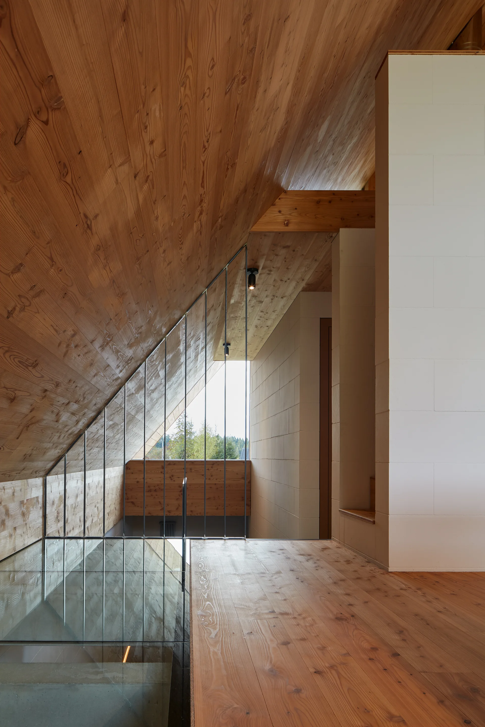 A modern staircase landing features a high sloped wood ceiling, vertical metal rod railings, and textured white masonry block walls.