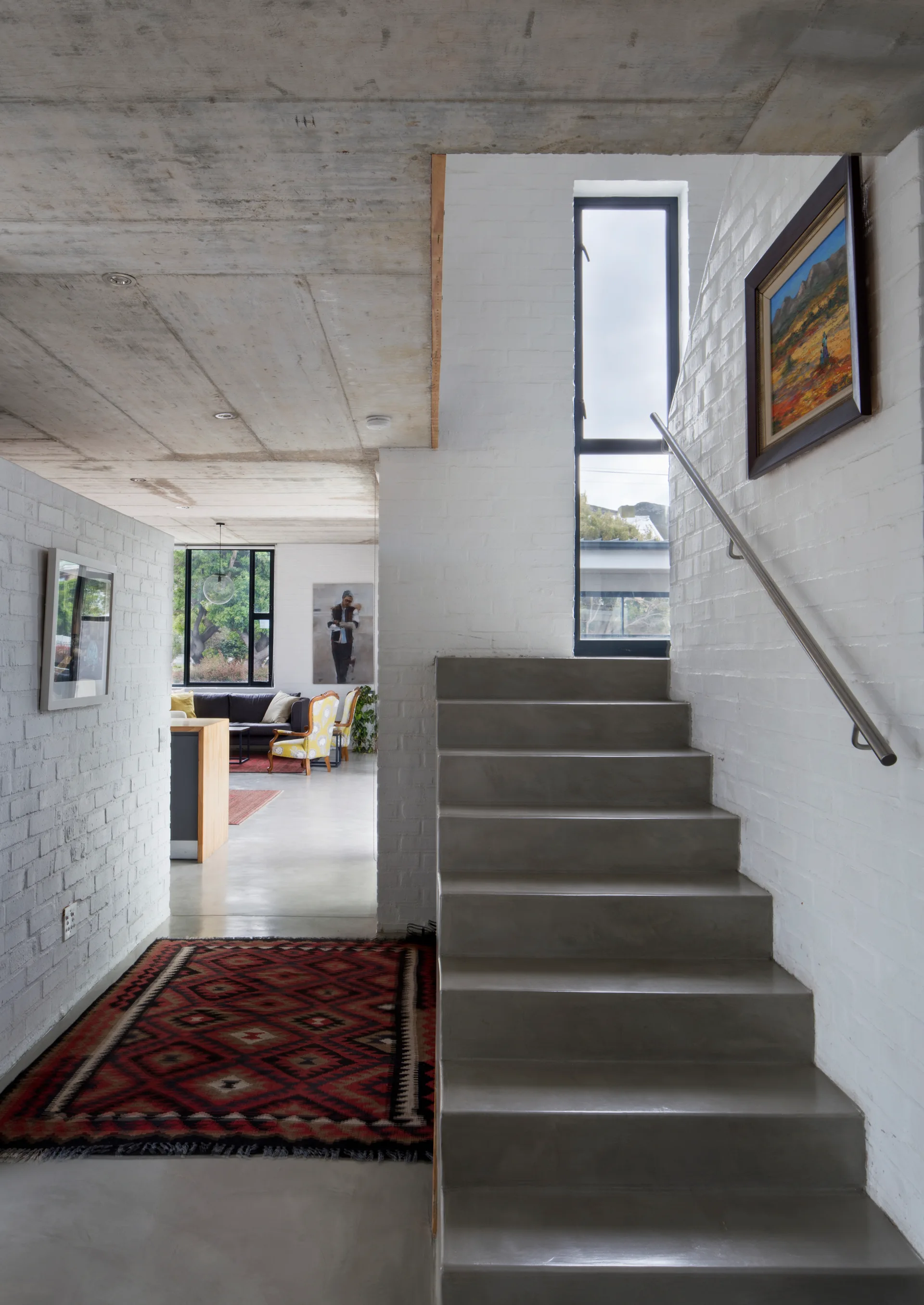 A minimalist hallway features a smooth concrete staircase next to painted white brick walls with a patterned runner on the floor.