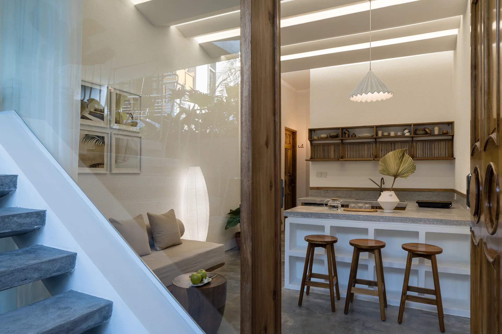An open-concept kitchen featuring a concrete island with wooden stools, a pleated pendant light, and a concrete staircase.