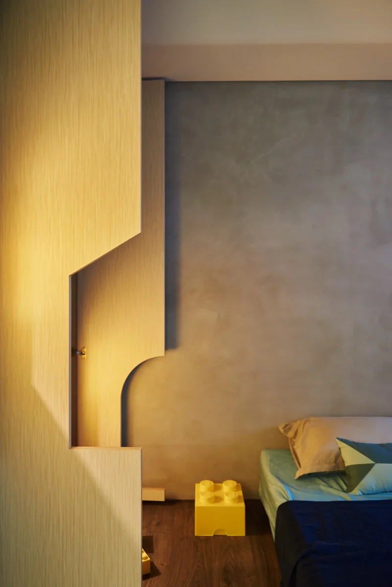 A modern bedroom features a textured grey wall behind a bed next to a custom light wood partition screen with a geometric cutout.