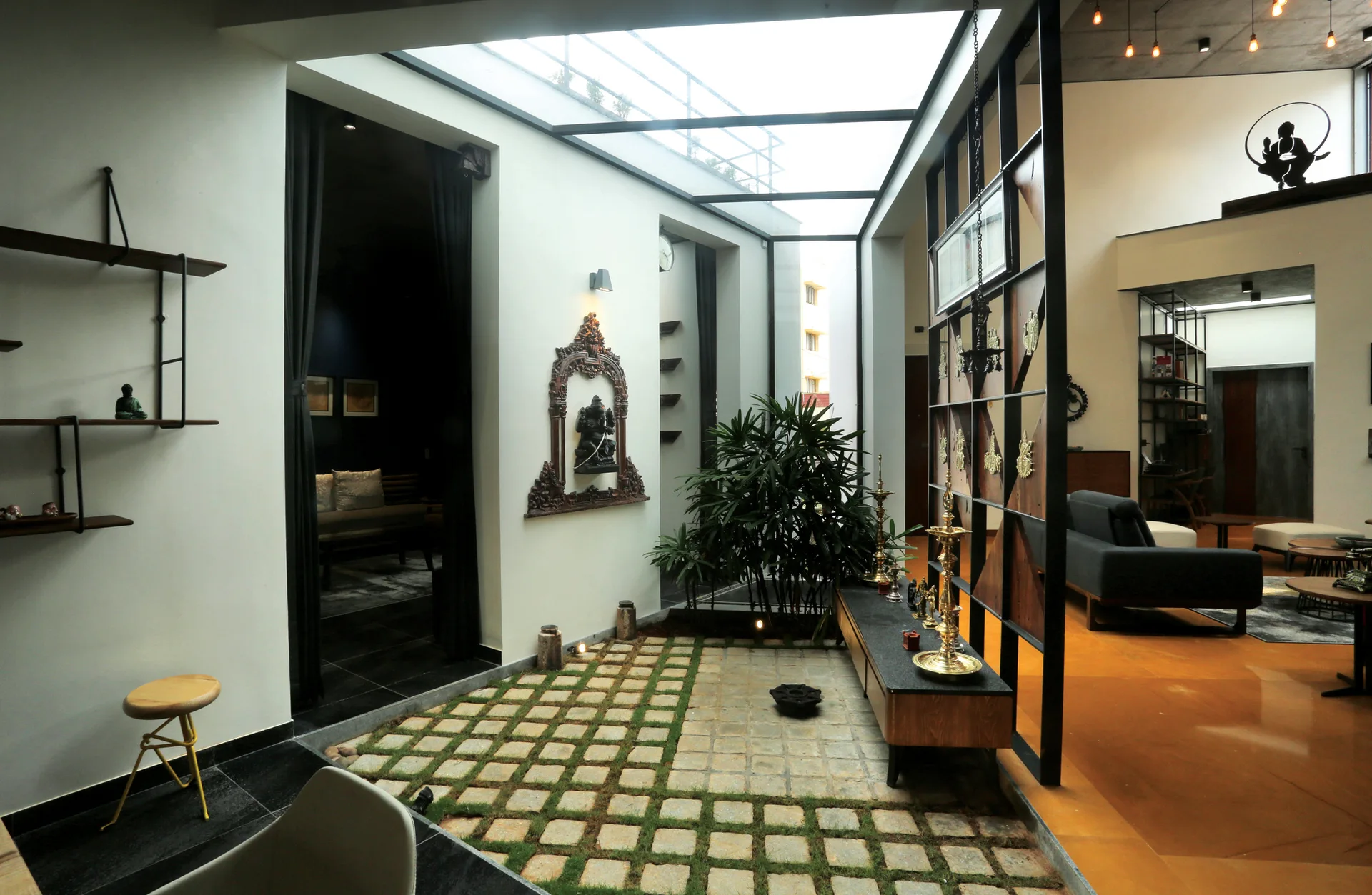 An indoor courtyard with stone and grass pavers under a glass skylight is flanked by a geometric wood partition and a living area.