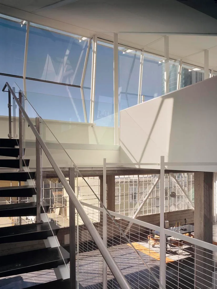 A multi-level interior featuring a black steel staircase, concrete columns, and upper level glass windows.