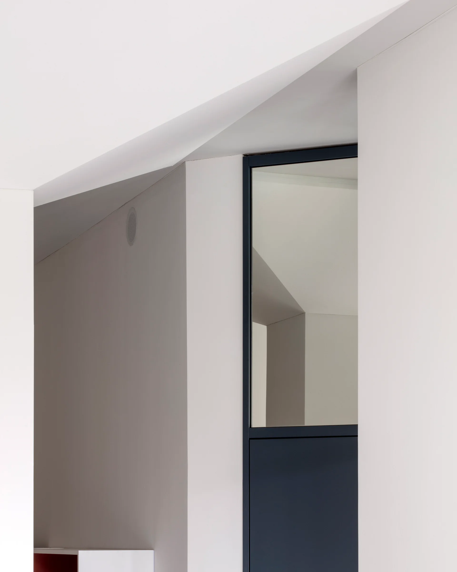 A minimalist modern interior featuring sharp angled white walls and a contrasting black-framed glass door component.