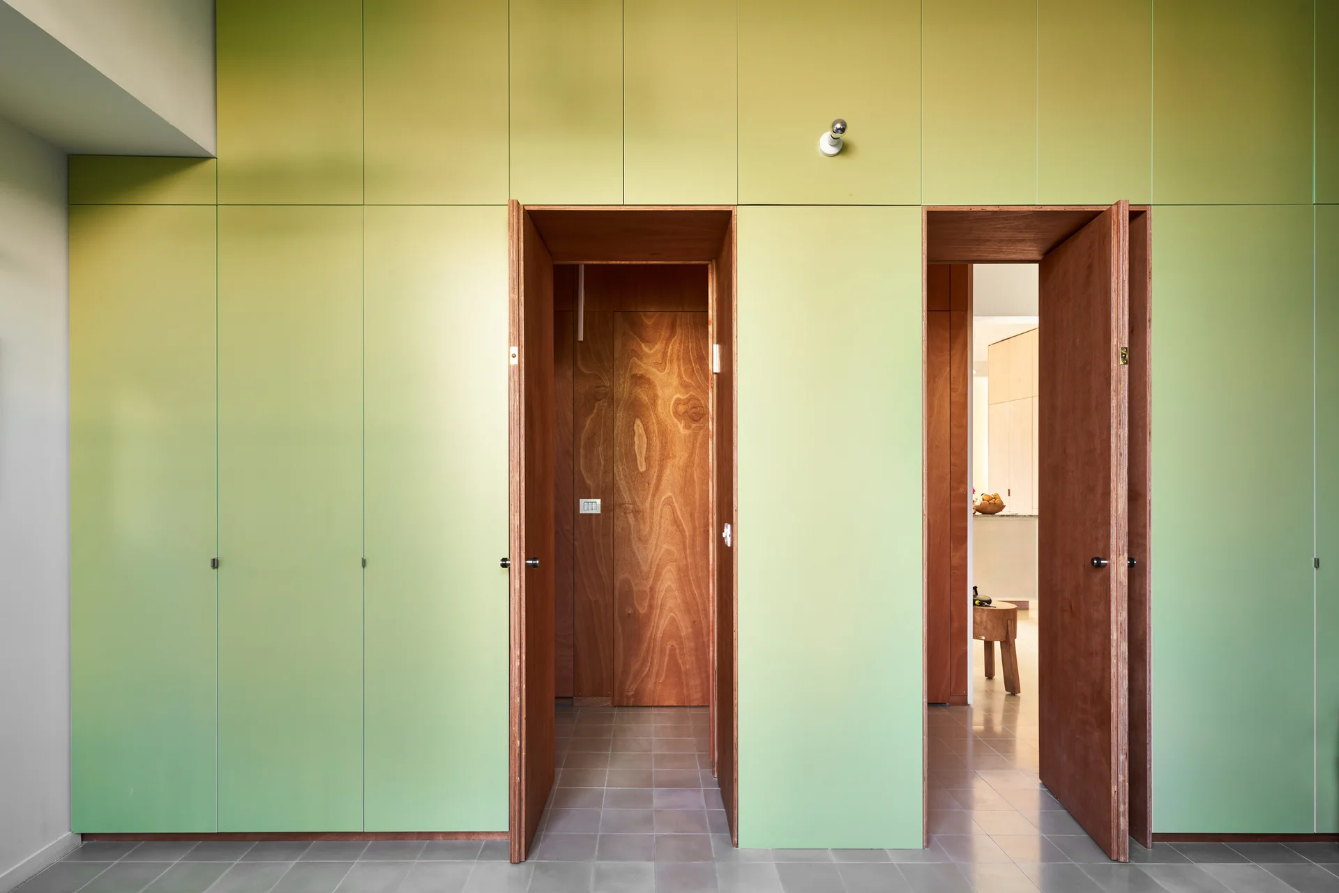 A pale green built-in storage wall features two open doorways lined with natural wood grain paneling over gray tiled flooring.