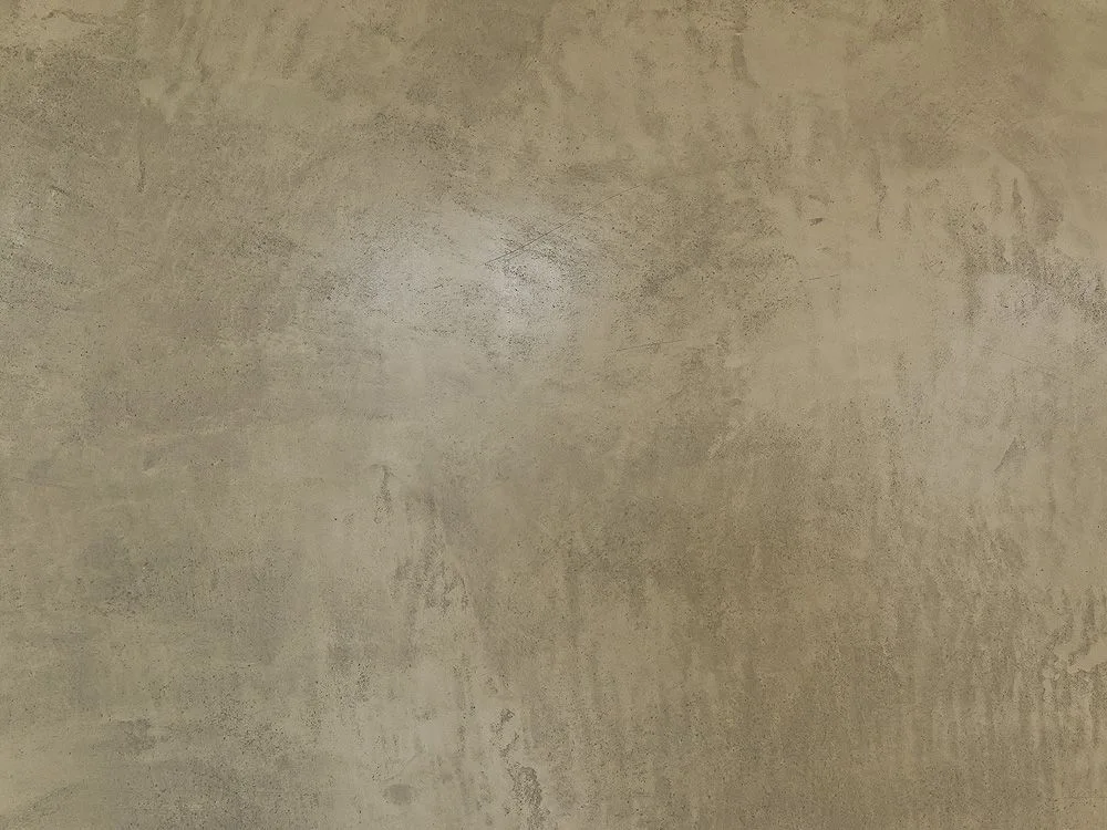 A close-up view of a matte plaster wall surface featuring mottled tan and grey tones with a subtle uneven texture.