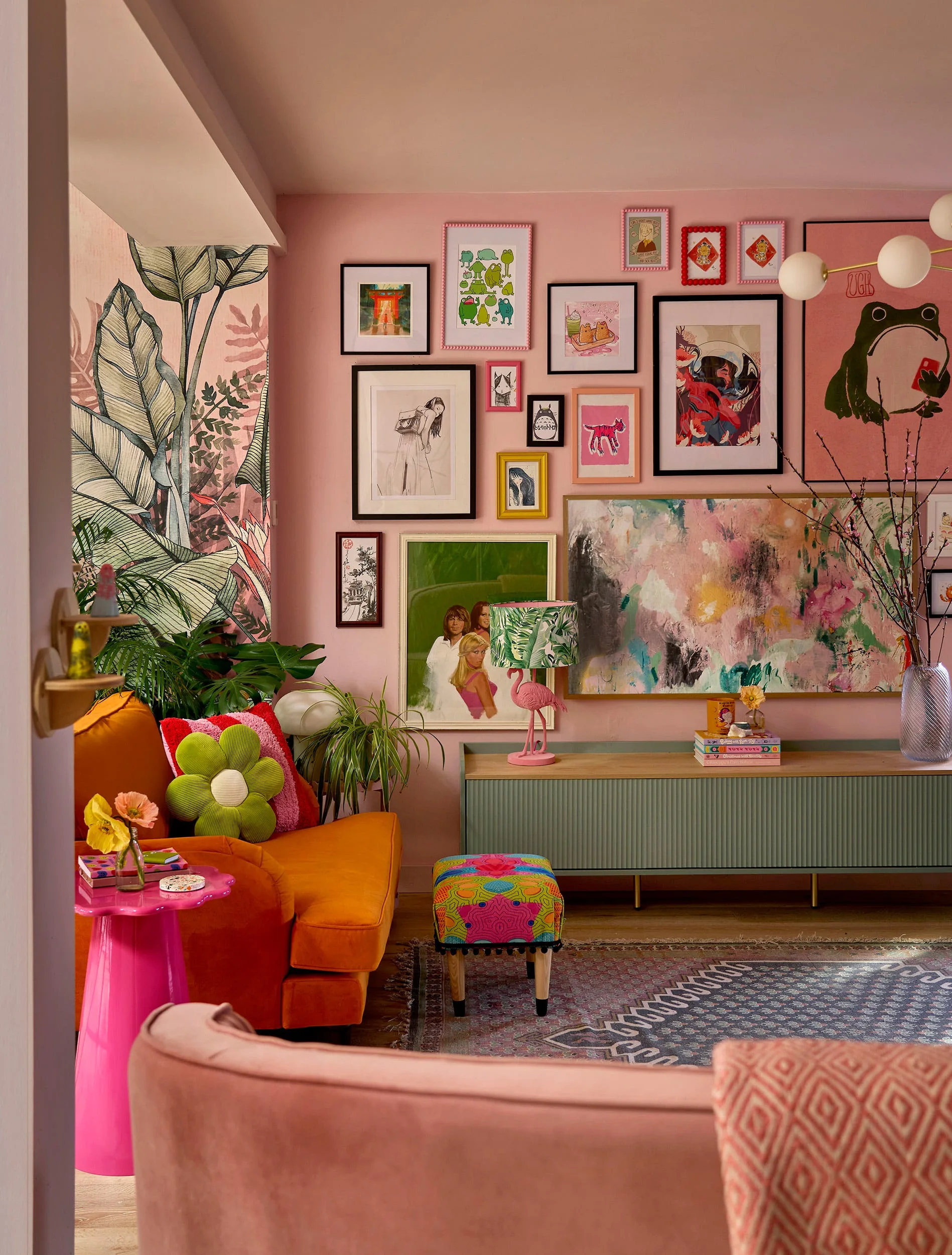 An eclectic pink living room features a green fluted sideboard beneath a dense gallery wall next to an orange armchair.